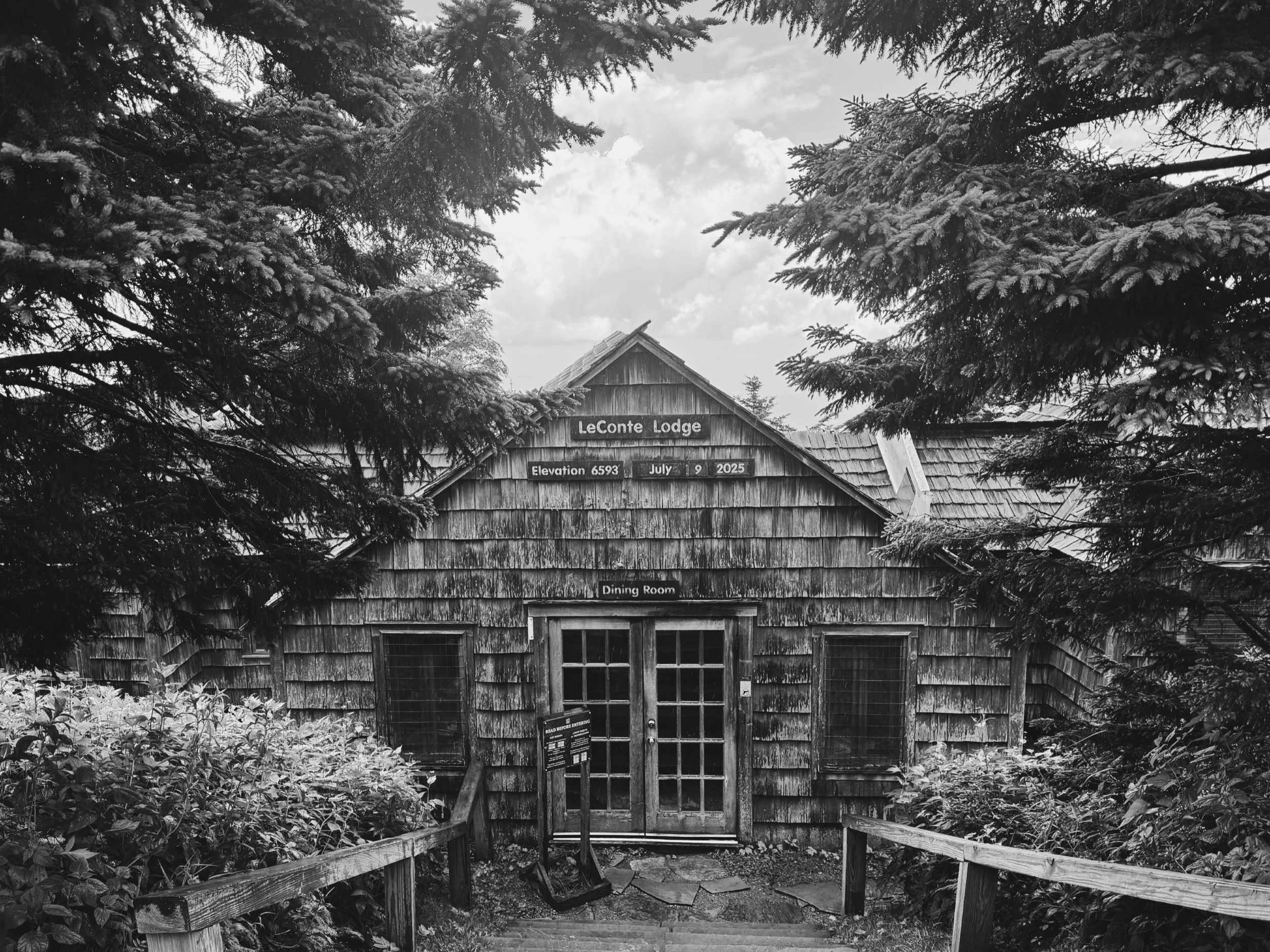 the dining room cabin at Leconte Lodge at the summit of mount Leconte is weathered and worn, surrounded by pine trees. the signs on the front read, "elevation 6593" and "July 9, 2025"