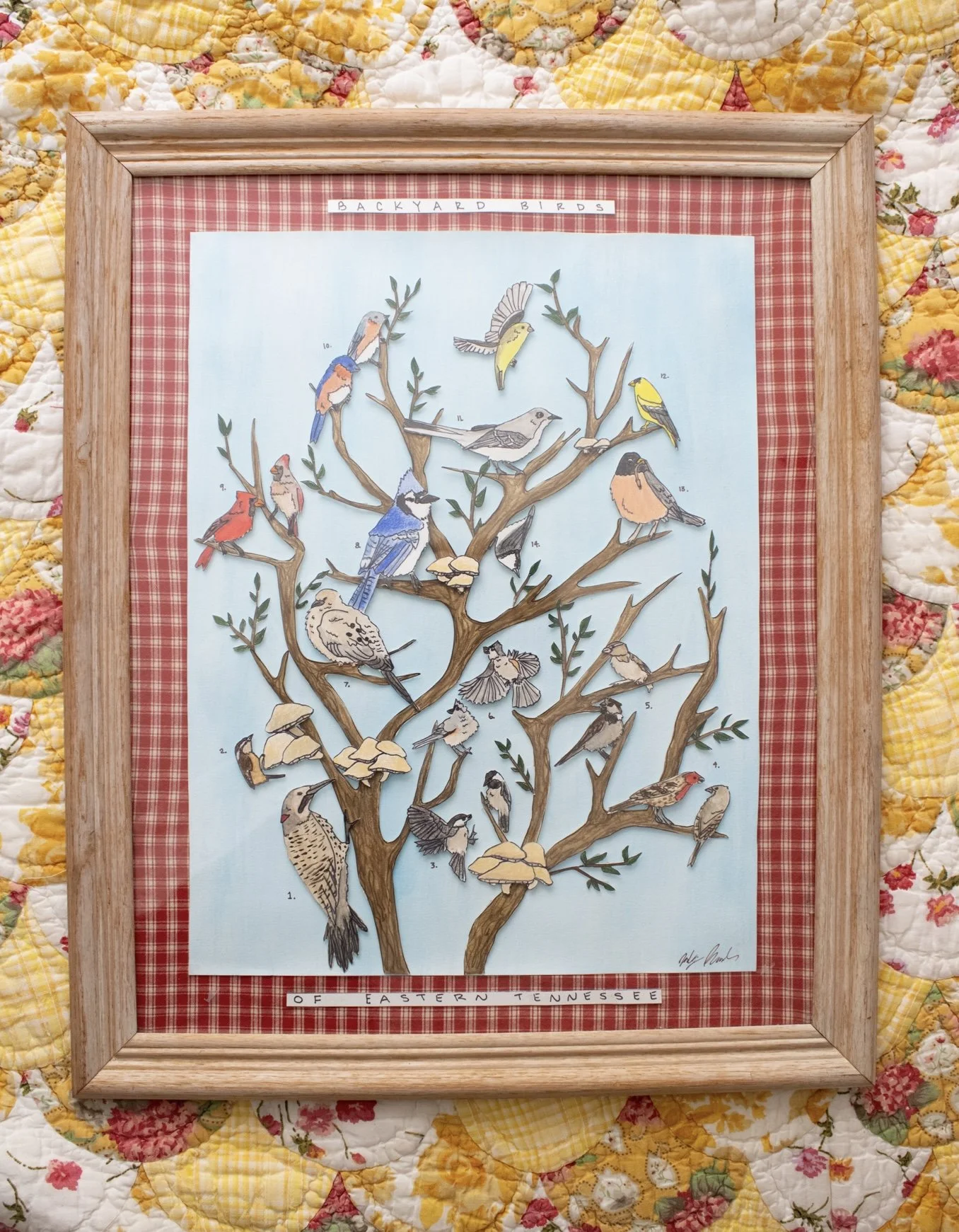 A poster style layered watercolor of backyard songbird species native to East Tennessee perched on tree branches against a sky blue background. It is framed with a red and white checkered matte in a light wood colored frame.