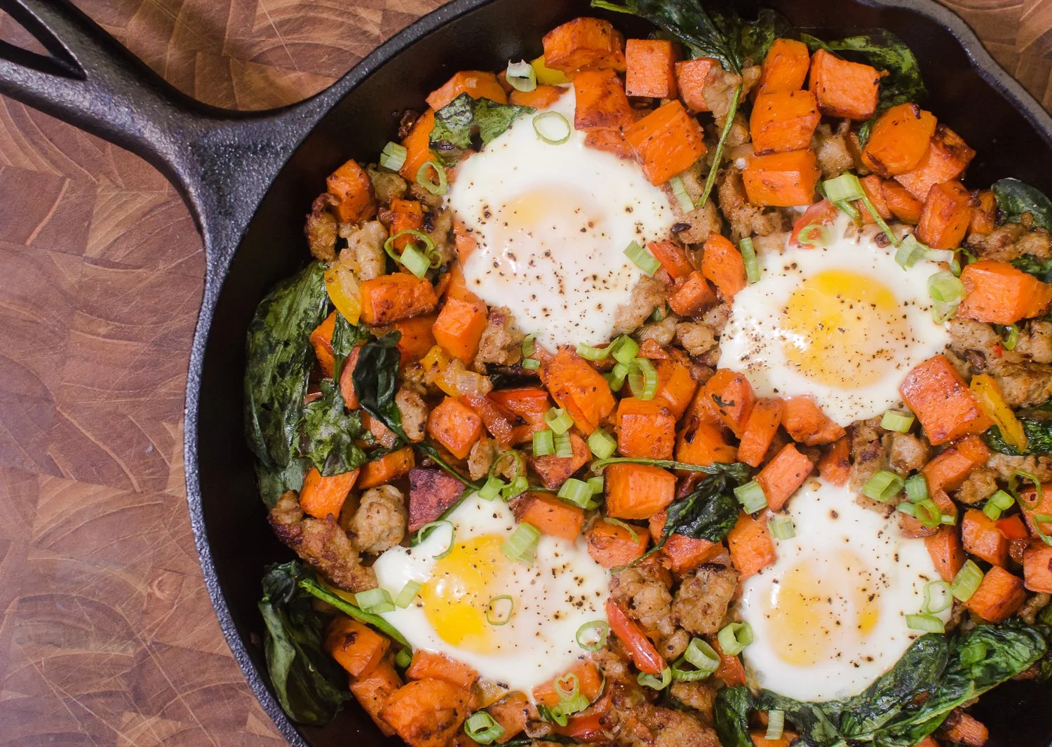Sweet potato and chorizo skillet made with Denmark Foods chorizo, topped with eggs and fresh greens, cooked in a cast iron pan and garnished with green onions.
