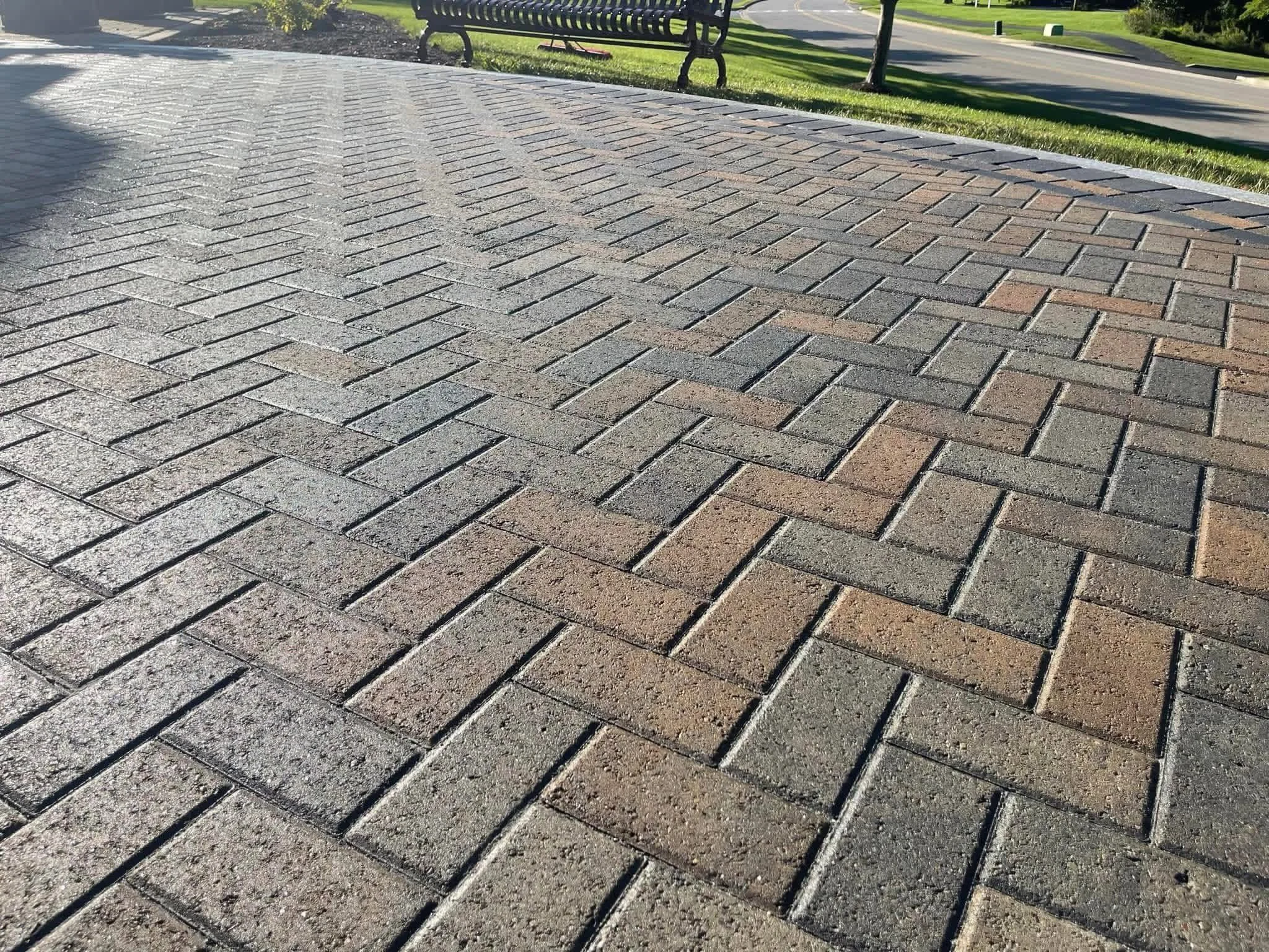 Close-up view of a brick pavement in a park with benches and green grass in the background.