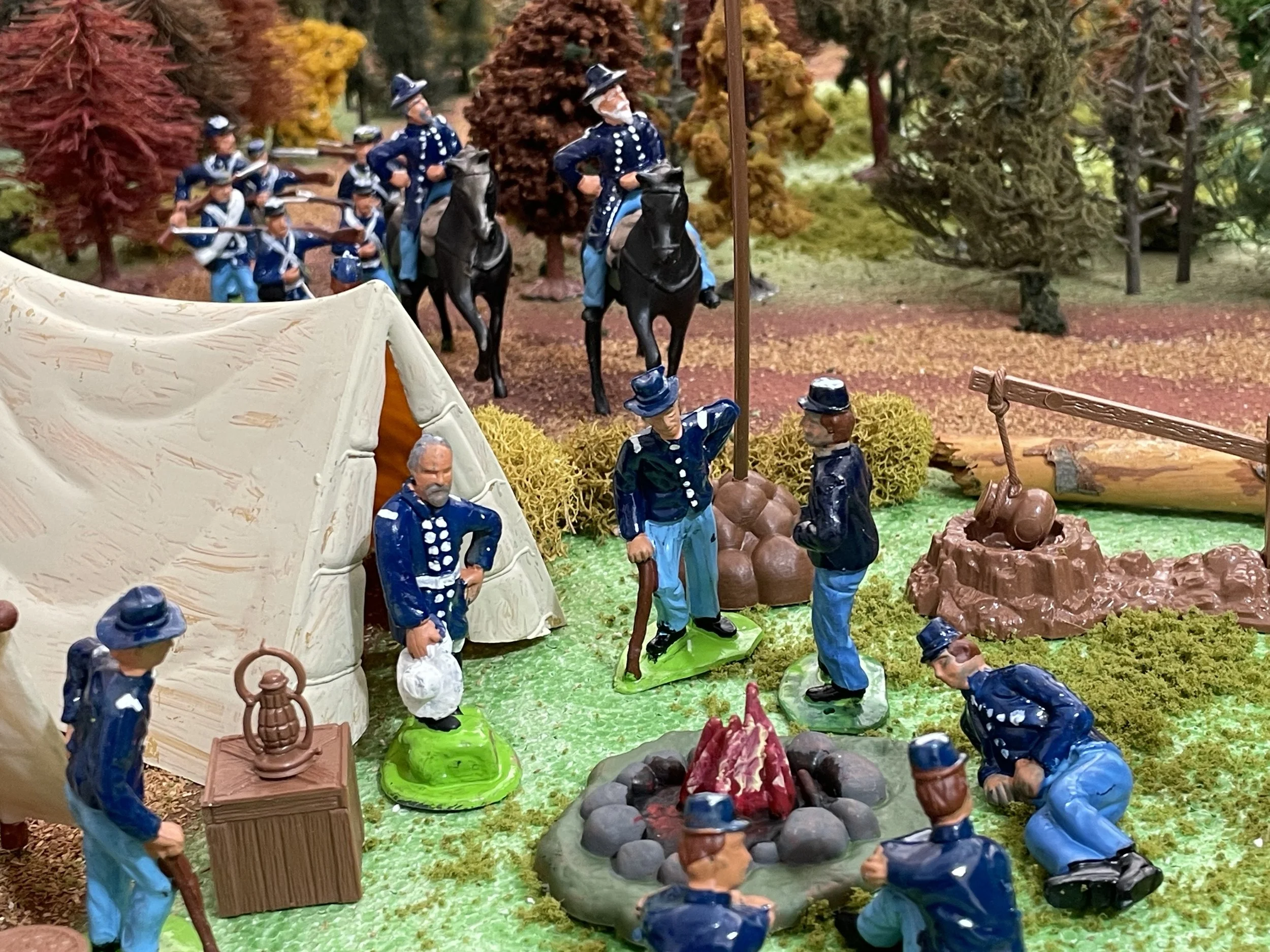 In the foreground, enlisted men gather around the evening fire — the social center of every Union camp. Meals, conversation, and quiet rest unfolded here after long days of drill or march. Behind them, mounted officers stand as a reminder that even m
