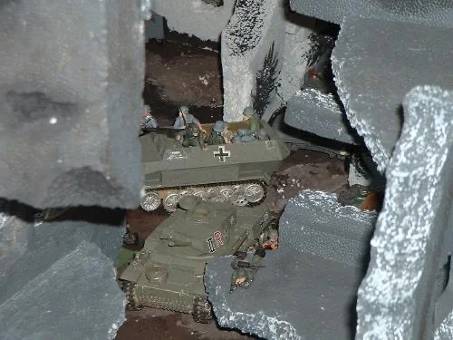 Tracked vehicles squeeze through the wreckage, scraping past walls that were once streets and homes.