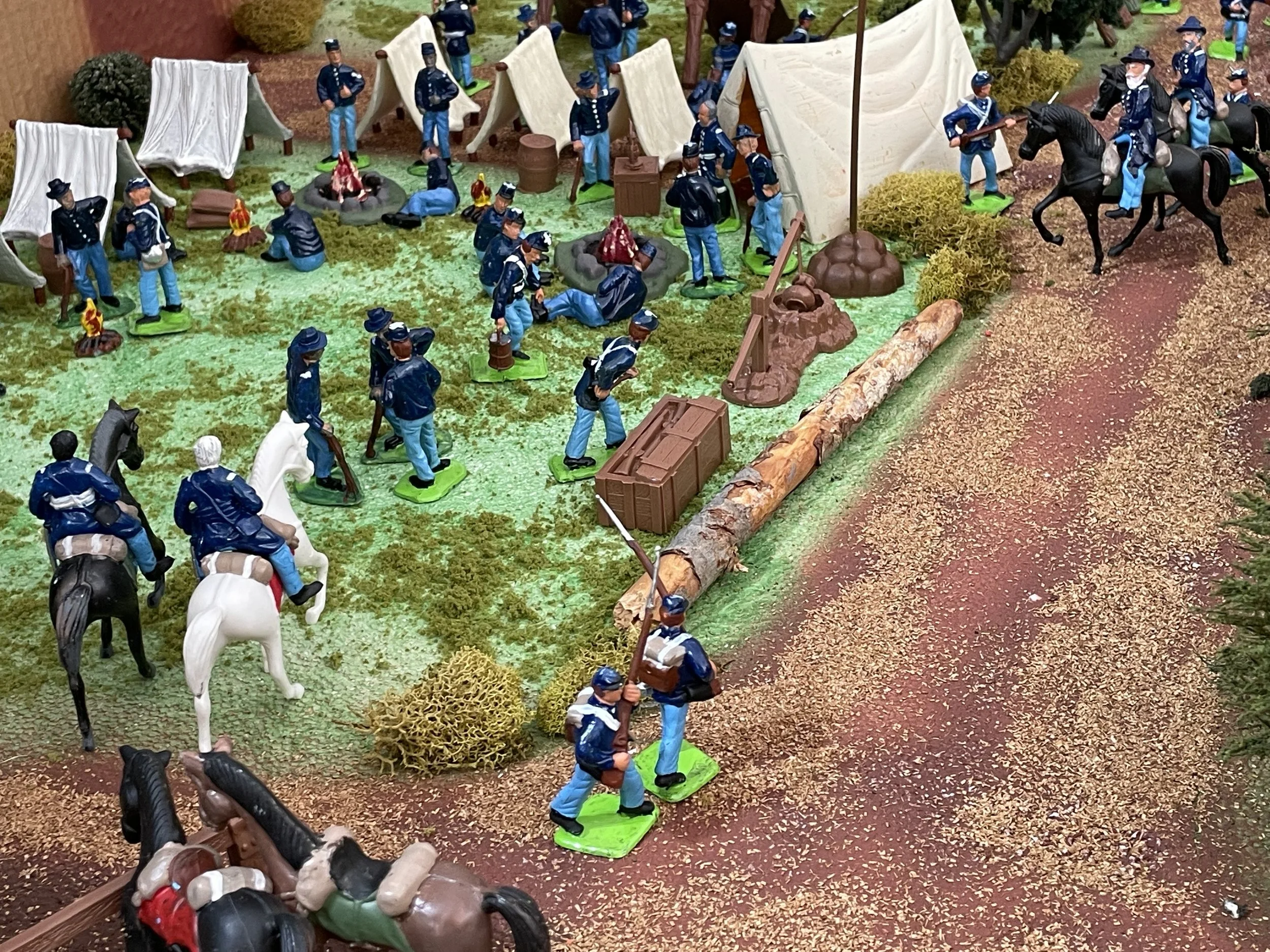 The camp bustles with quiet purpose as dawn approaches. Riders confer near the road, infantry shoulder muskets, and fatigue details move crates and timber into place. Orders have come — whether march, drill, or engagement — and the stillness of night