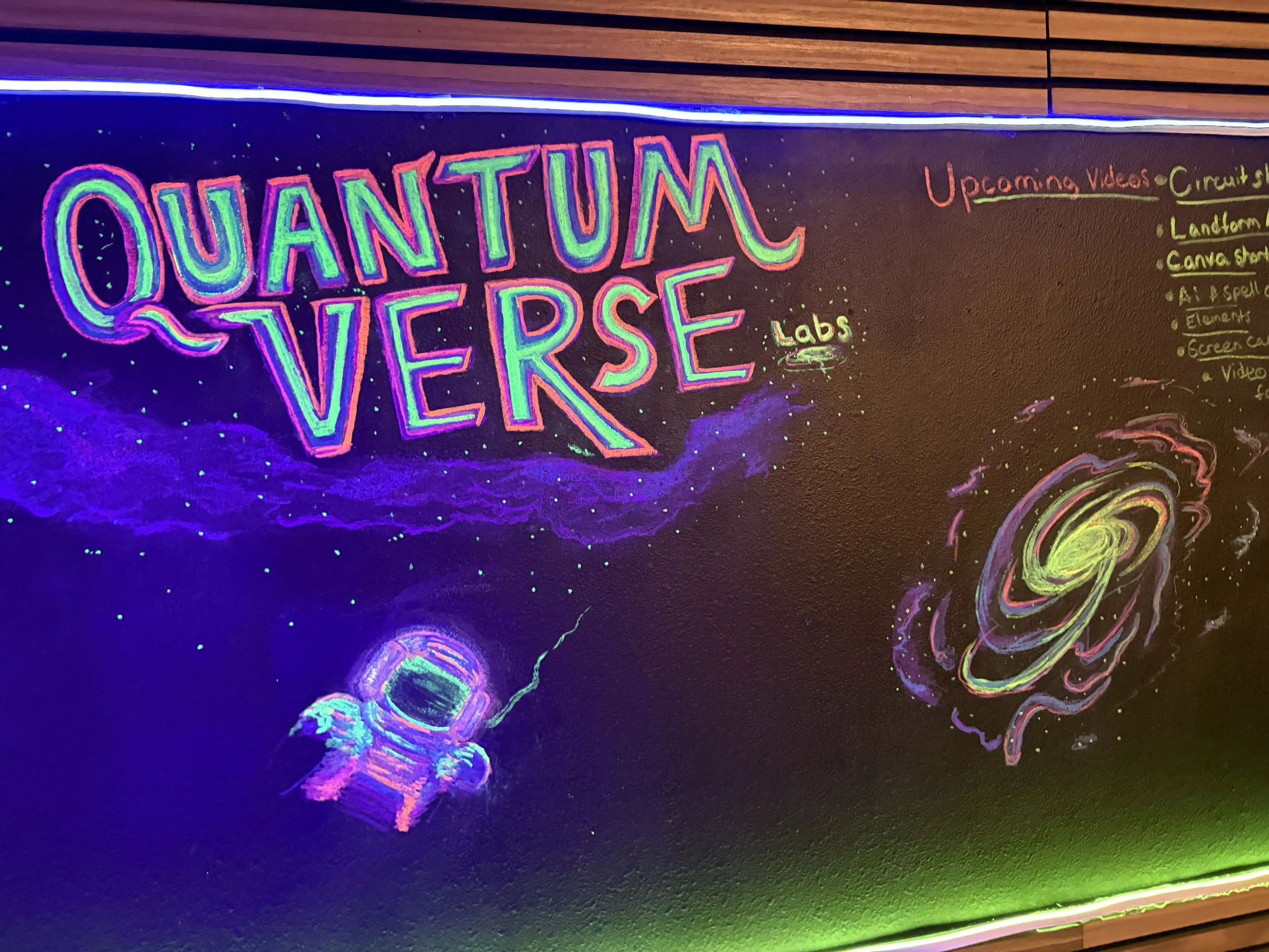 Neon chalkboard display featuring the words 'Quantum Verse' in colorful lettering, an illustrated astronaut, a swirling galaxy, and notes about future projects.