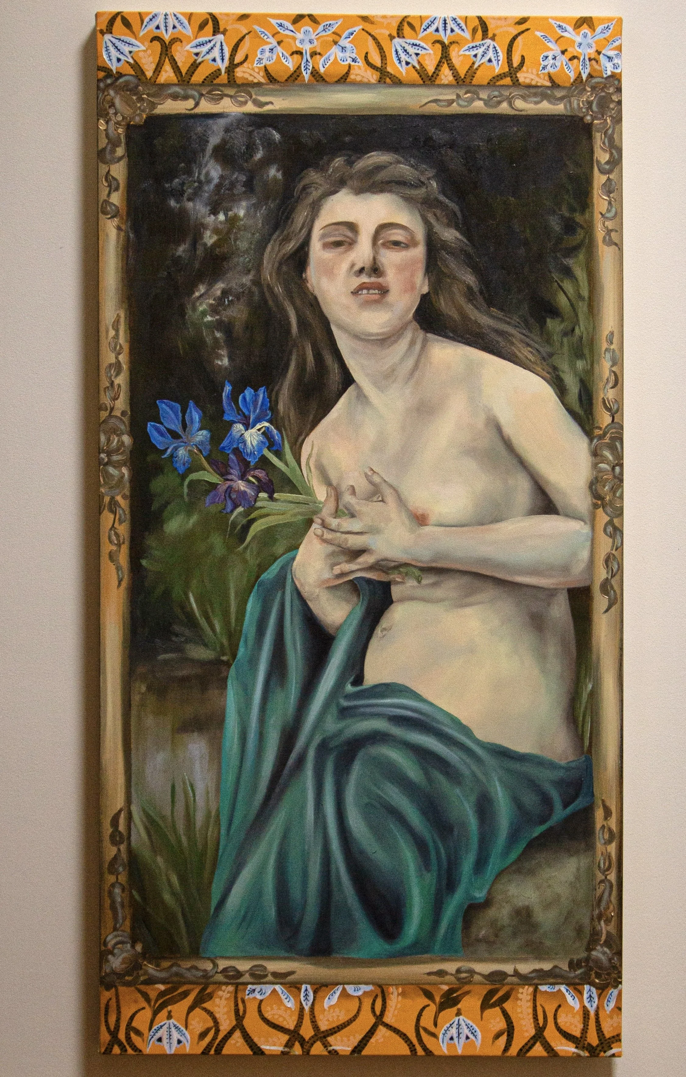 A painting of a woman with long, wavy hair, holding a small bouquet of blue and purple irises, draped in a dark teal cloth, with a dark background and a decorative orange and blue patterned border.