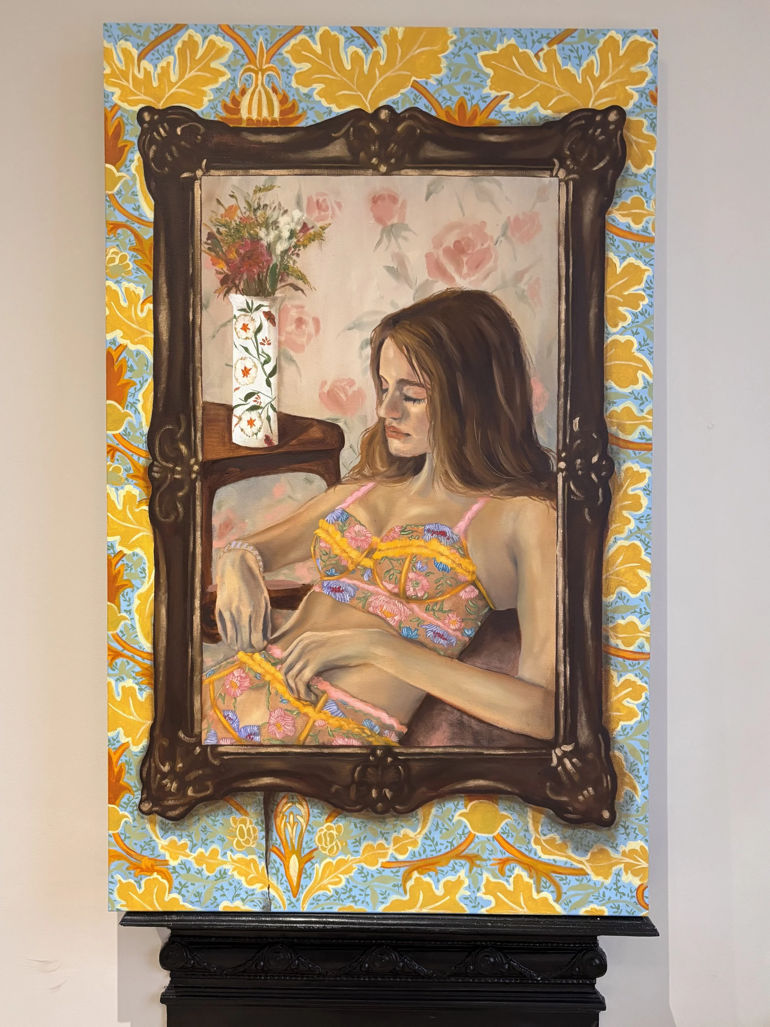 A painting of a young woman with long brown hair wearing colorful lingerie, sitting on a dark piece of furniture. She is surrounded by a decorative frame and a background of pink roses and floral wallpaper, with a vase of flowers on a side table.