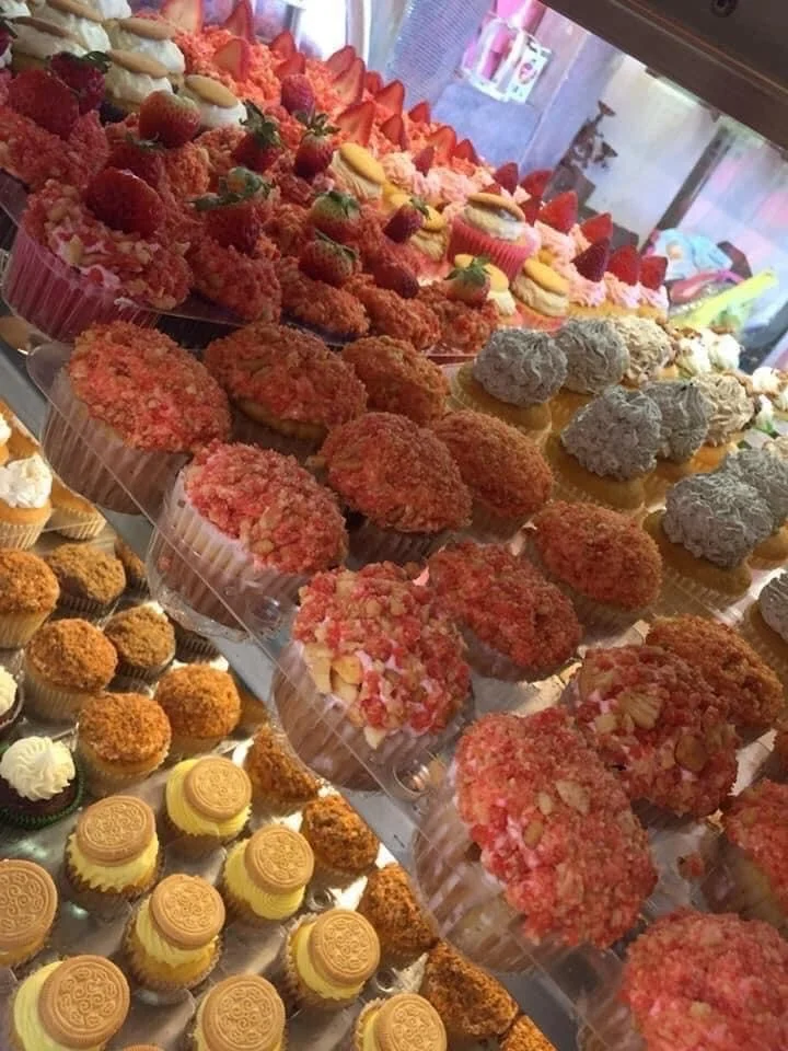 A display case filled with a variety of desserts including strawberries, cupcakes, cookies, and other sweet treats.