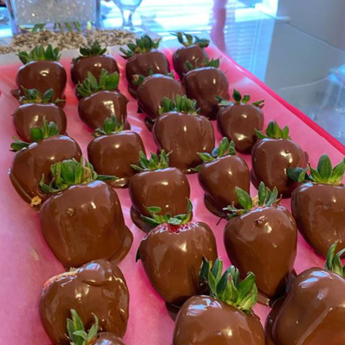Chocolate-covered strawberries arranged on pink paper.