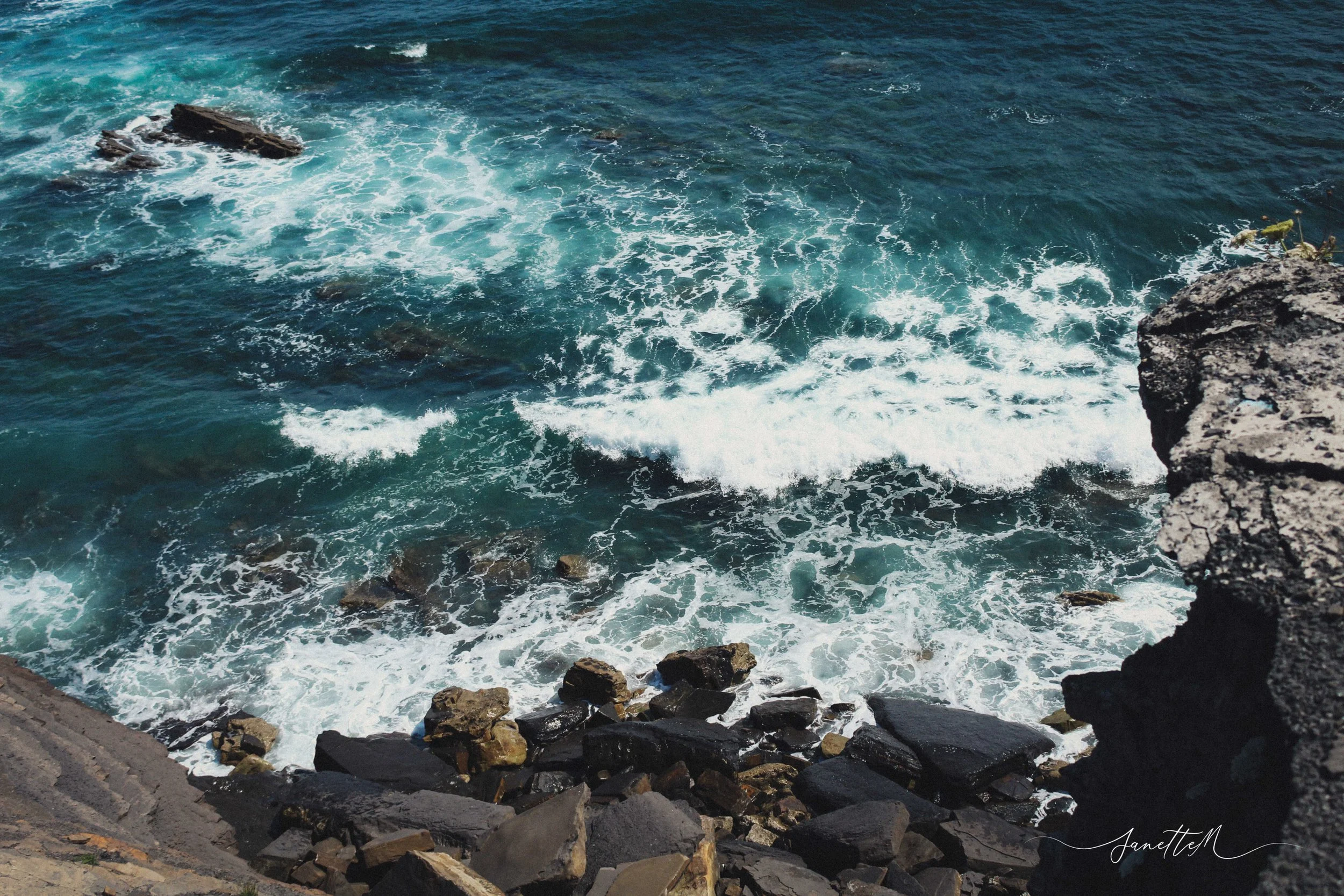 Vista desde un acantilado sobre el océano con olas rompiendo contra rocas oscuras.