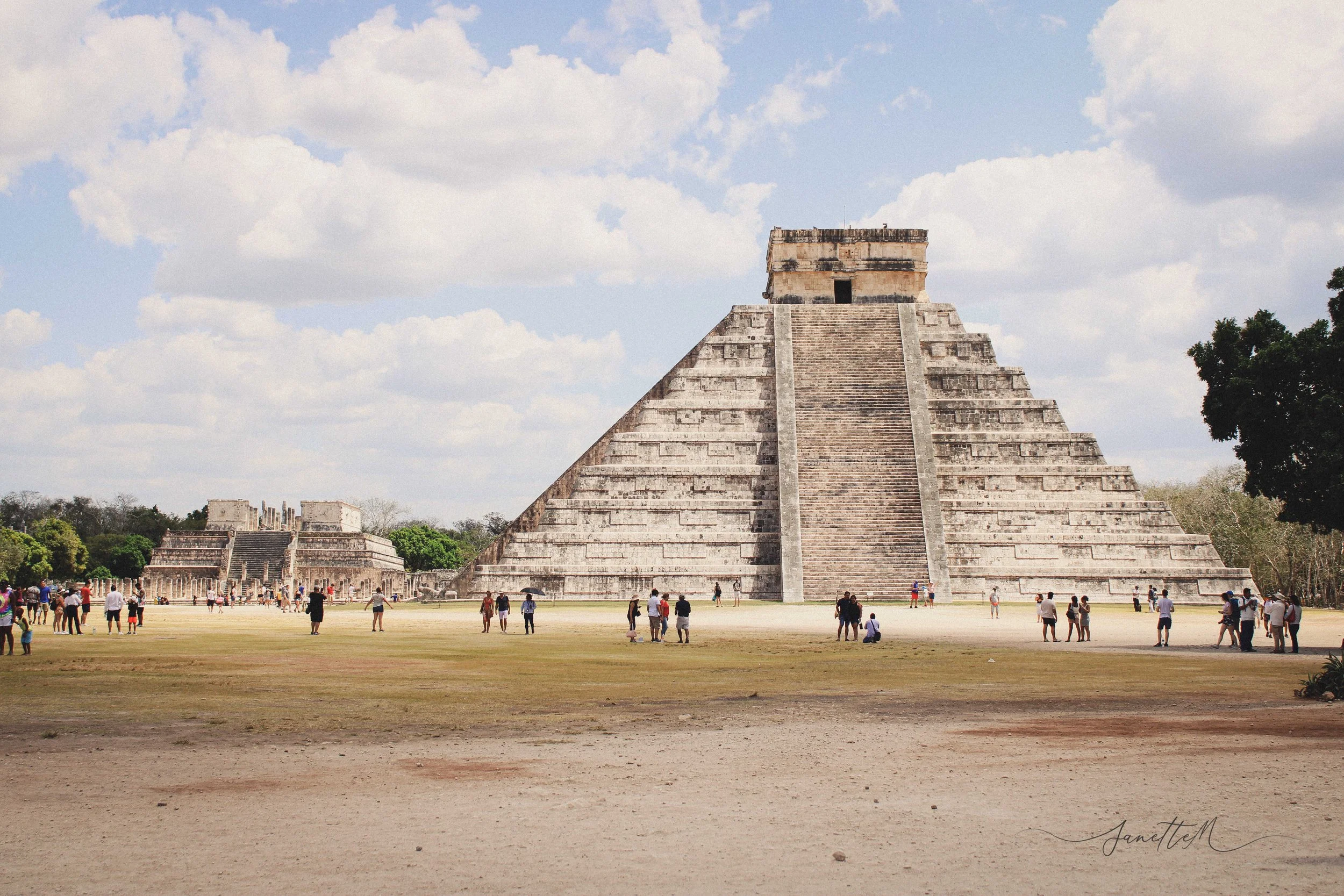 Una pirámide maya en un sitio arqueológico, con muchas personas visitándola, bajo un cielo nublado.