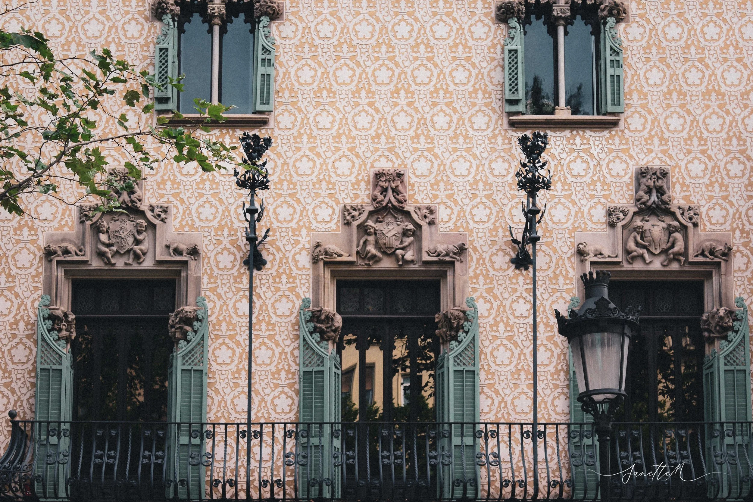 Barcelona - Edificio con fachada decorada con azulejos, ventanas con retranque y aberturas verdes, letrero de farol de calle y decoración escultórica en la fachada.