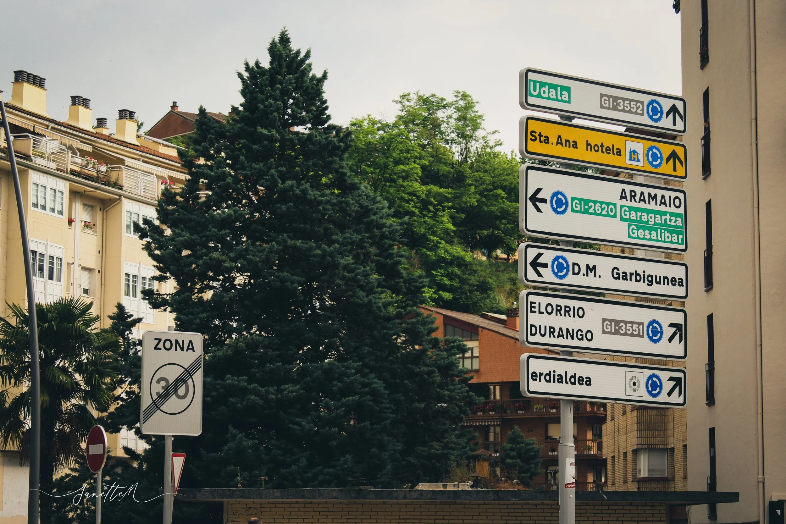 Señales de tráfico y direccionales en una calle con árboles y edificios en el fondo