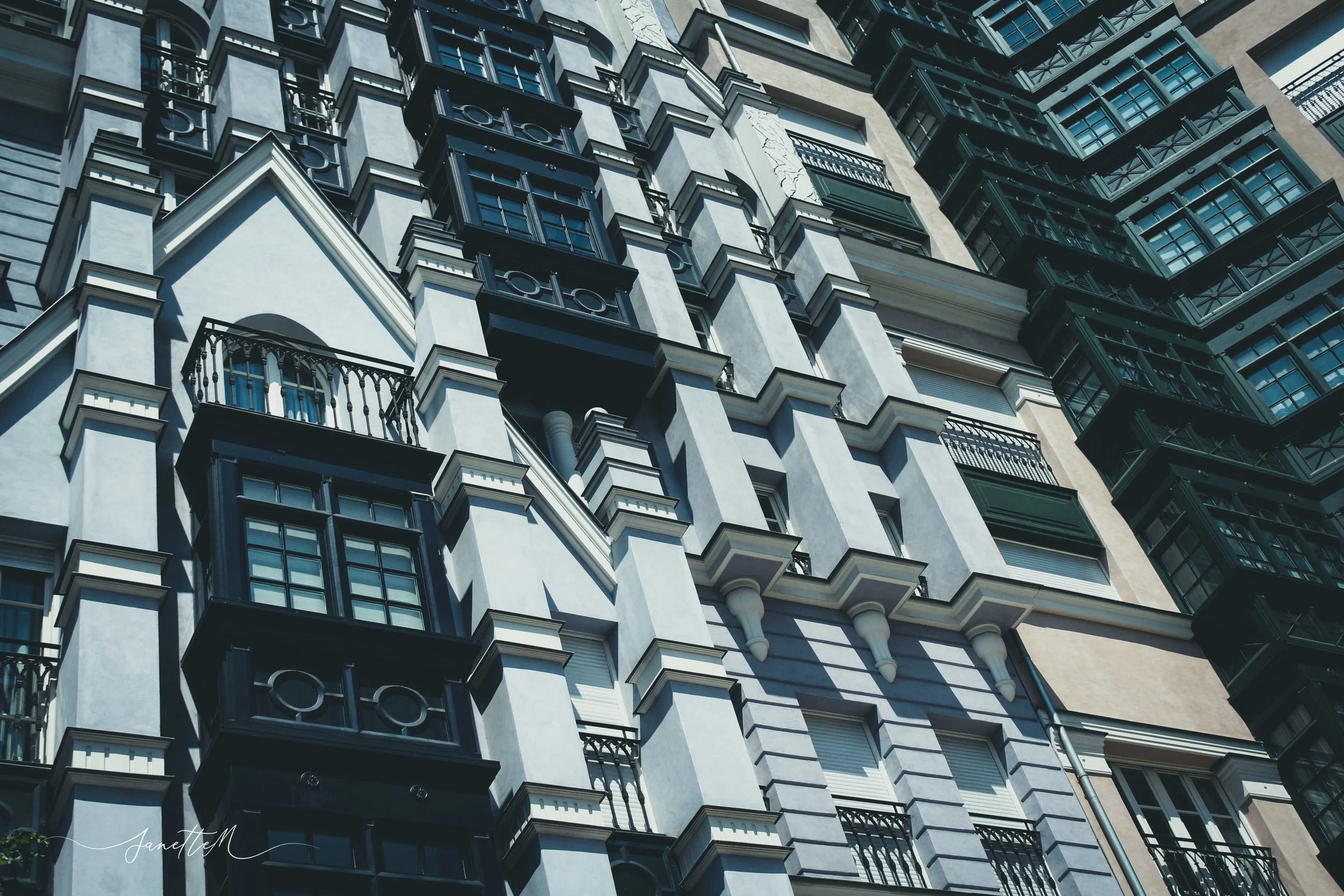 Edificio de apartamentos con muchas ventanas y balcones. Fachada de color claro con detalles en negro y vigas de metal en los balcones.