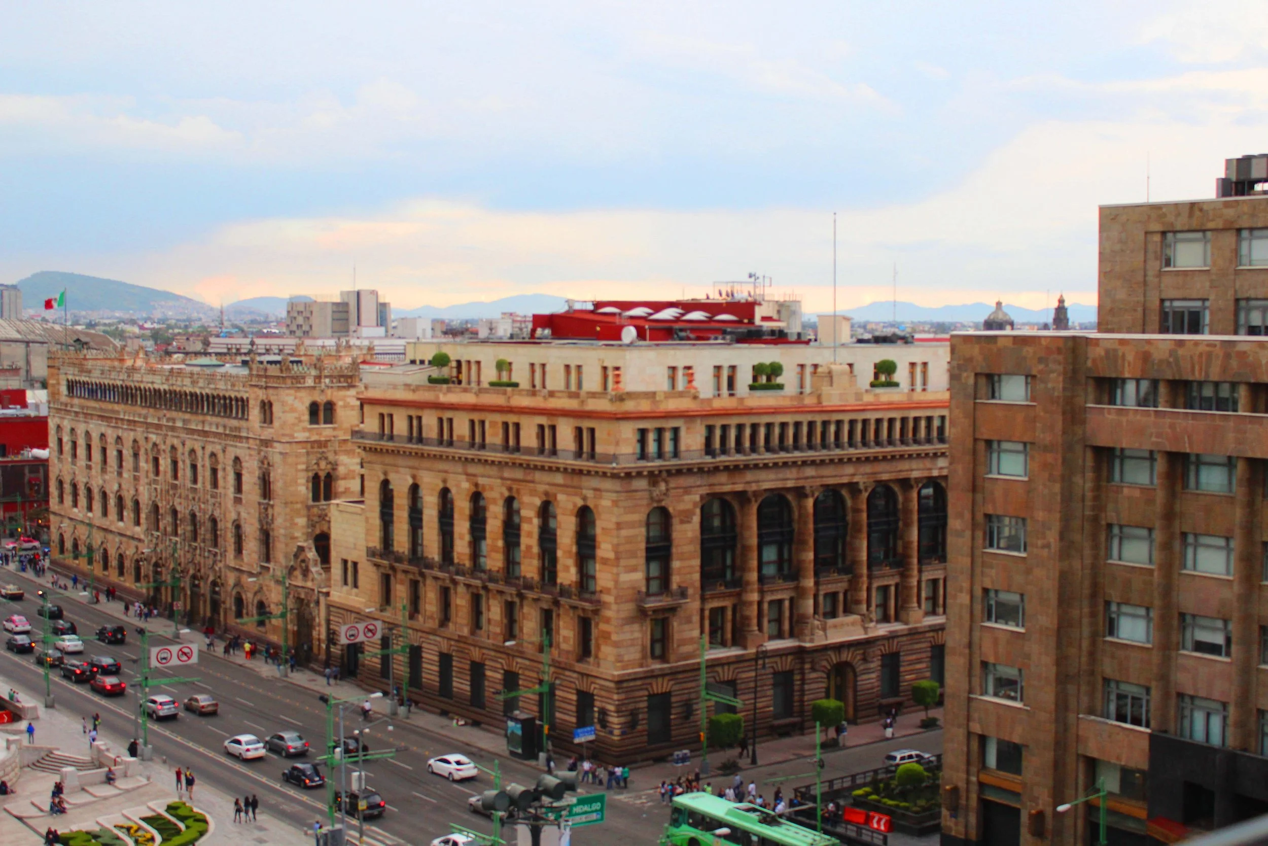 Vista urbana en la ciudad con edificios históricos y modernas calles llenas de autos y peatones, en un día nublado.