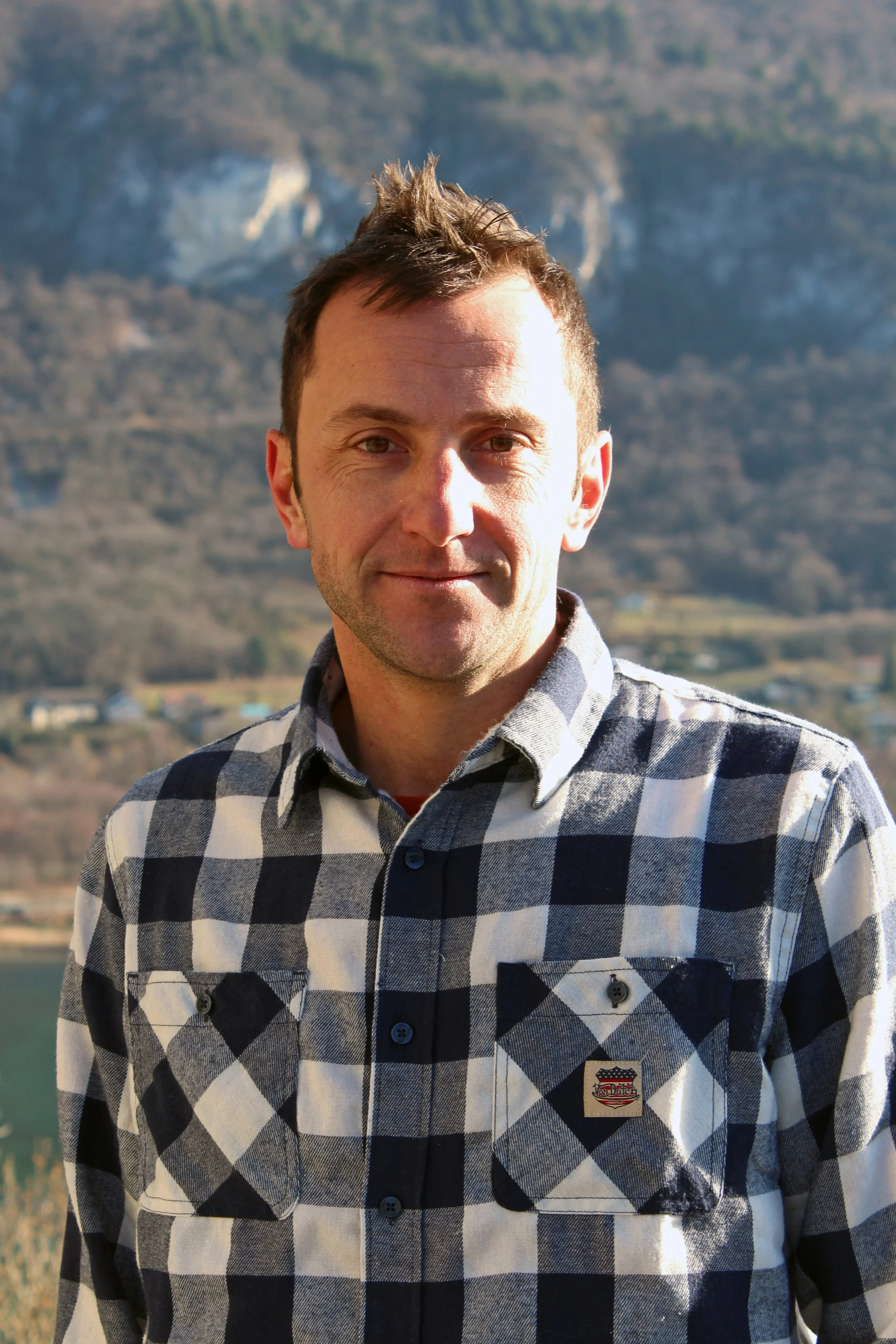 Un homme de Chindrieux portant une chemise à carreaux noir et blanc, avec un paysage de montagne en arrière-plan.
