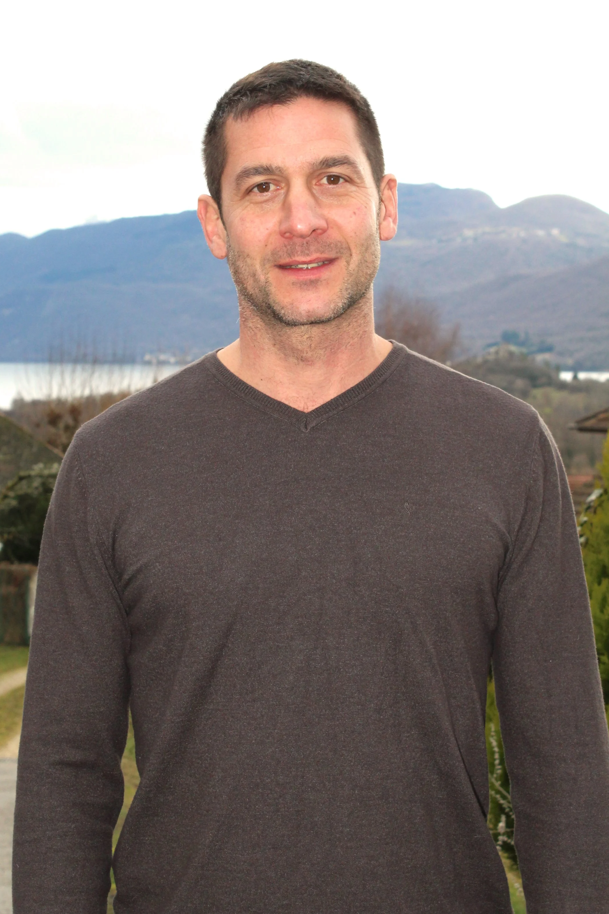 Un homme de Chindrieux avec une veste marron clair se tient devant un paysage de montagnes et de végétation.