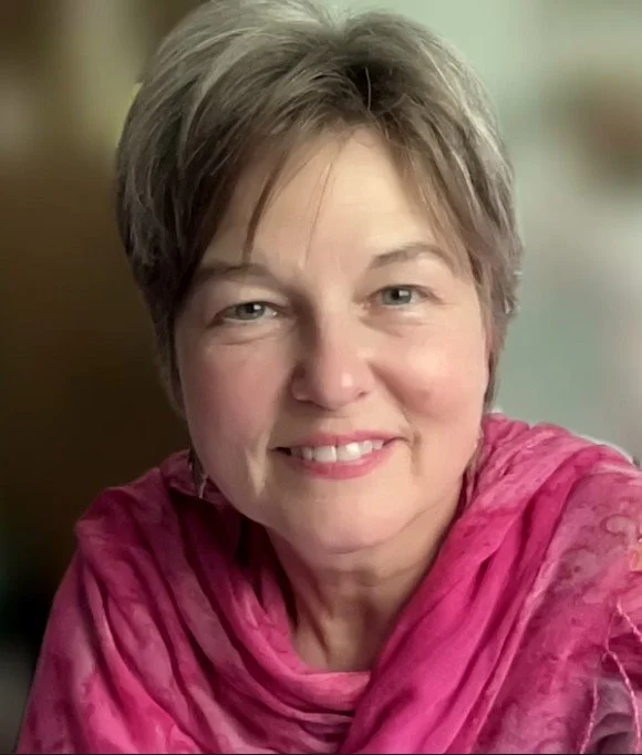 A middle-aged woman with short hair, smiling, wearing a pink scarf.