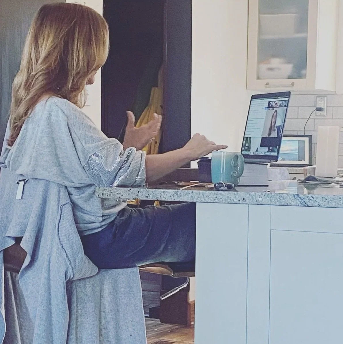 A woman sitting at a kitchen counter engaged in a video call on her laptop.