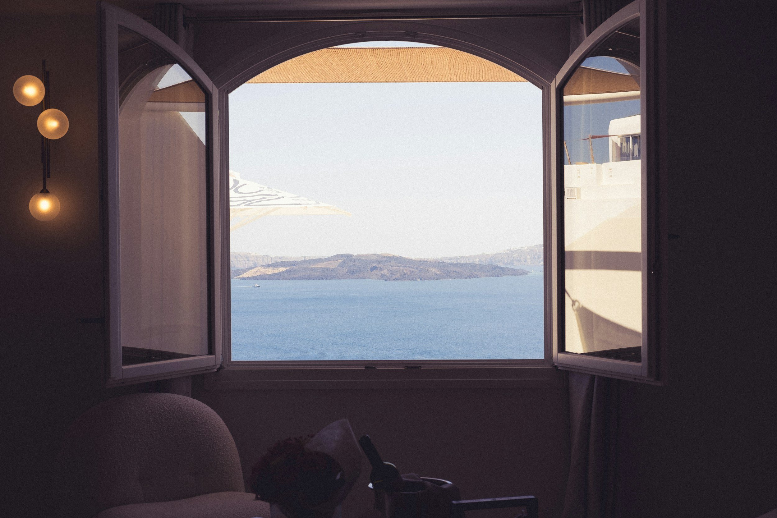Arched, wooden window frame. Windows are open overlooking a Seaview with a warm light fixture on the left.