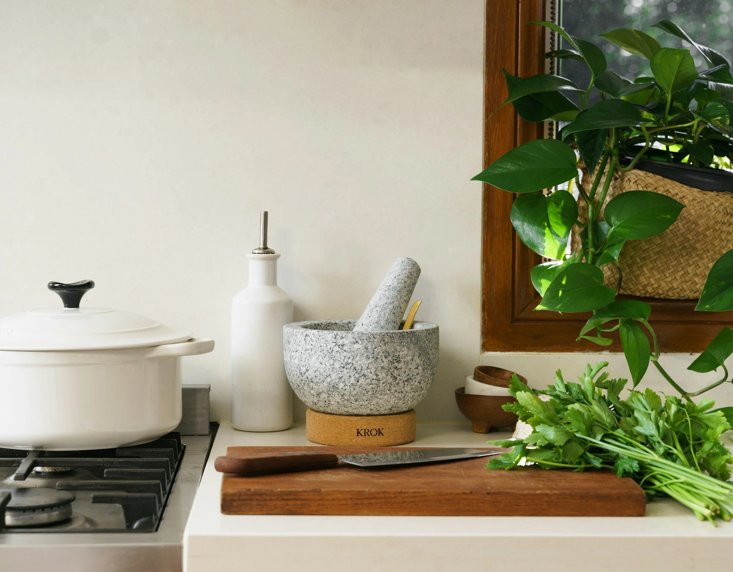 Biophilic kitchen with wooden chopping board and knife. Ceramic pan on the left and pestle and mortar in stone.
