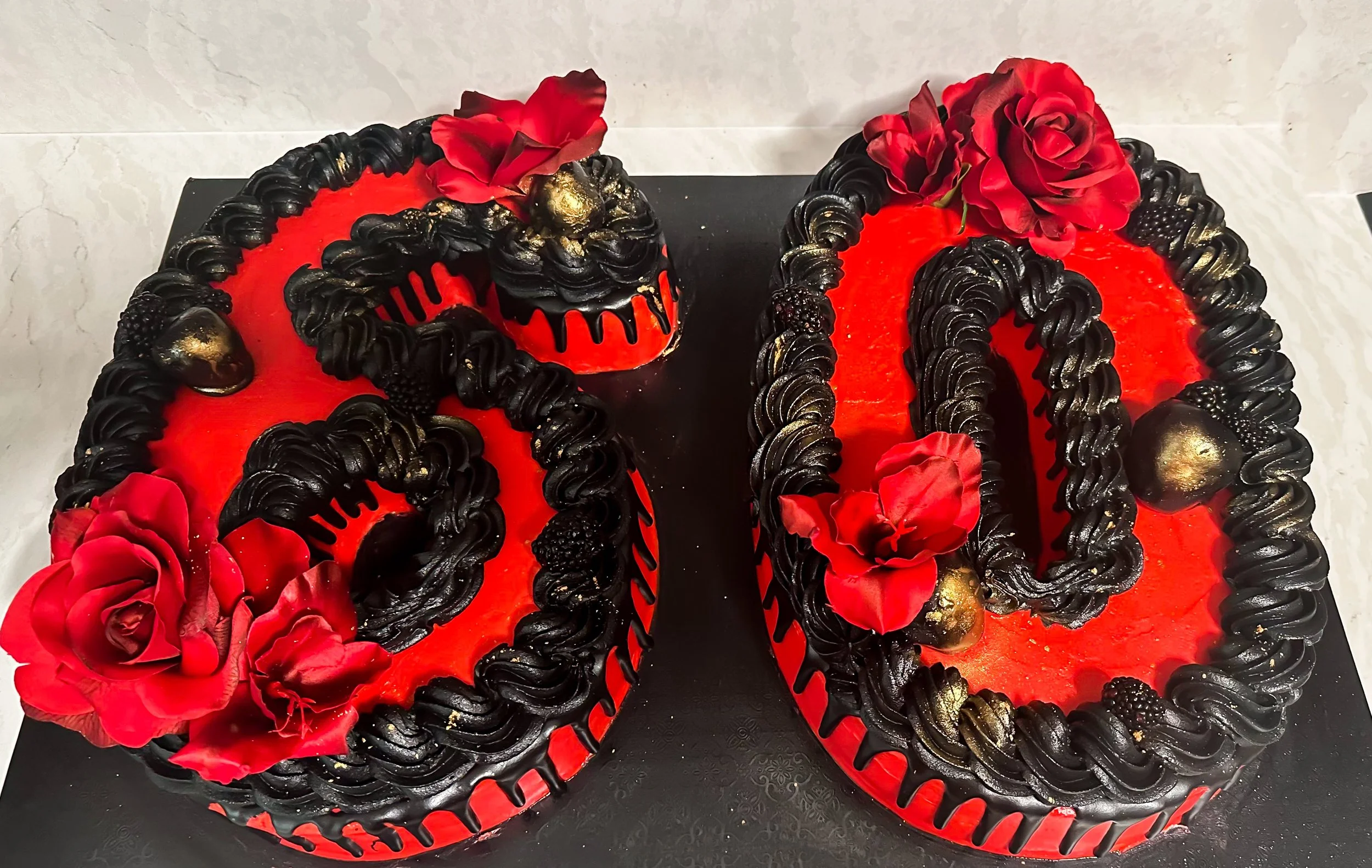 A birthday cake in the shape of the number 30, decorated with black frosting, red flowers, and gold accents.