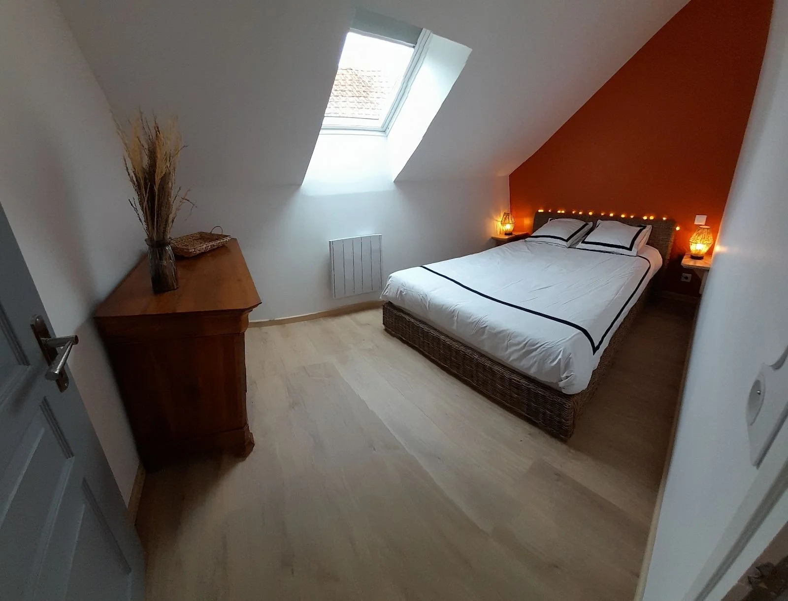 Chambre avec lit double en bois tressé, lampes de chevet, fenêtre de toit, décoration mince et lumineuse.