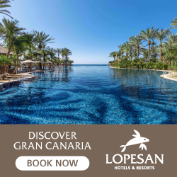 A resort pool area overlooking the ocean, surrounded by palm trees and clear blue sky