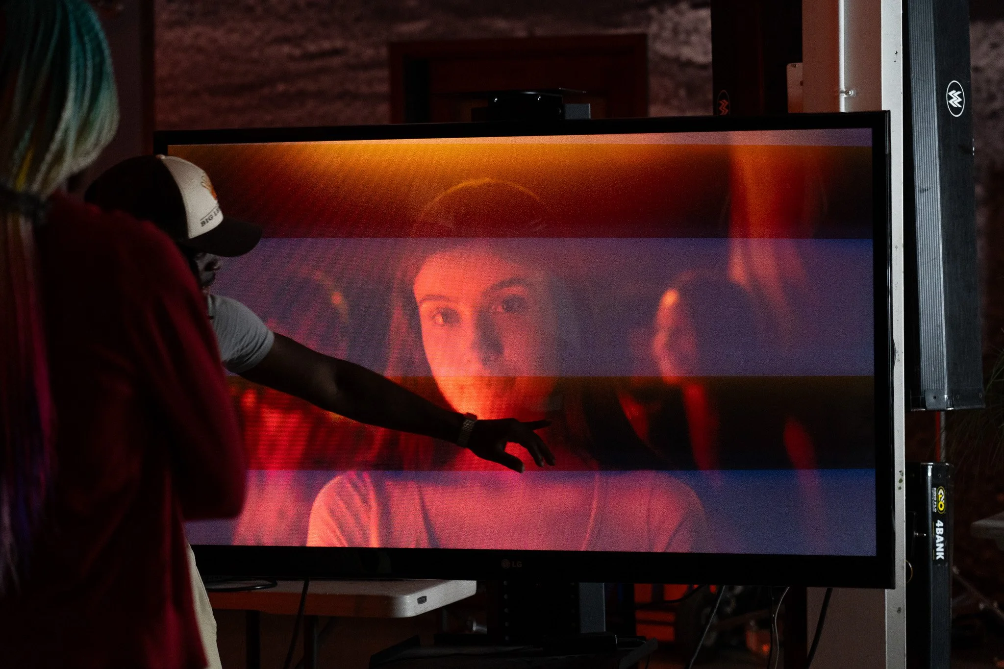 A person pointing at a large screen displaying a woman's face with two horizontal lines across the image.