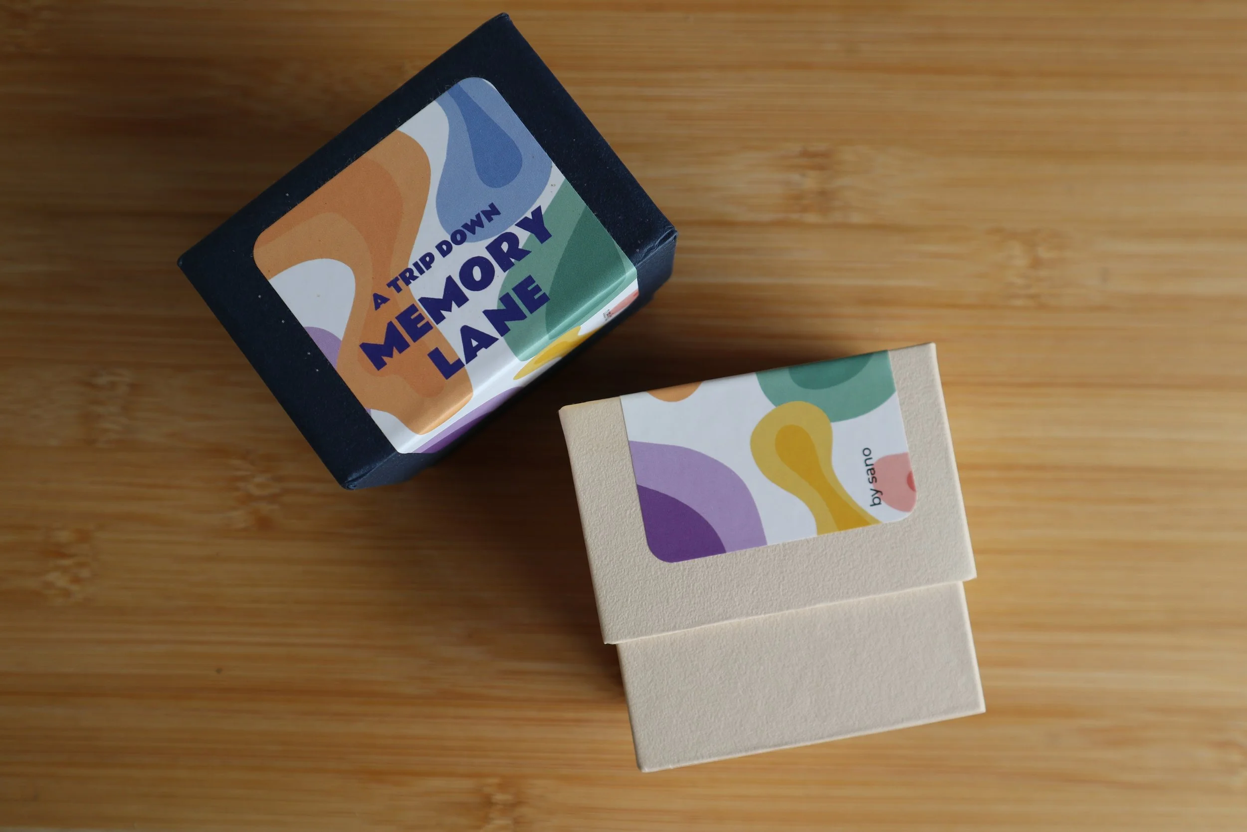 Two boxes with colorful abstract patterns on them, one with a dark background and the other with a light background, placed on a wooden surface.