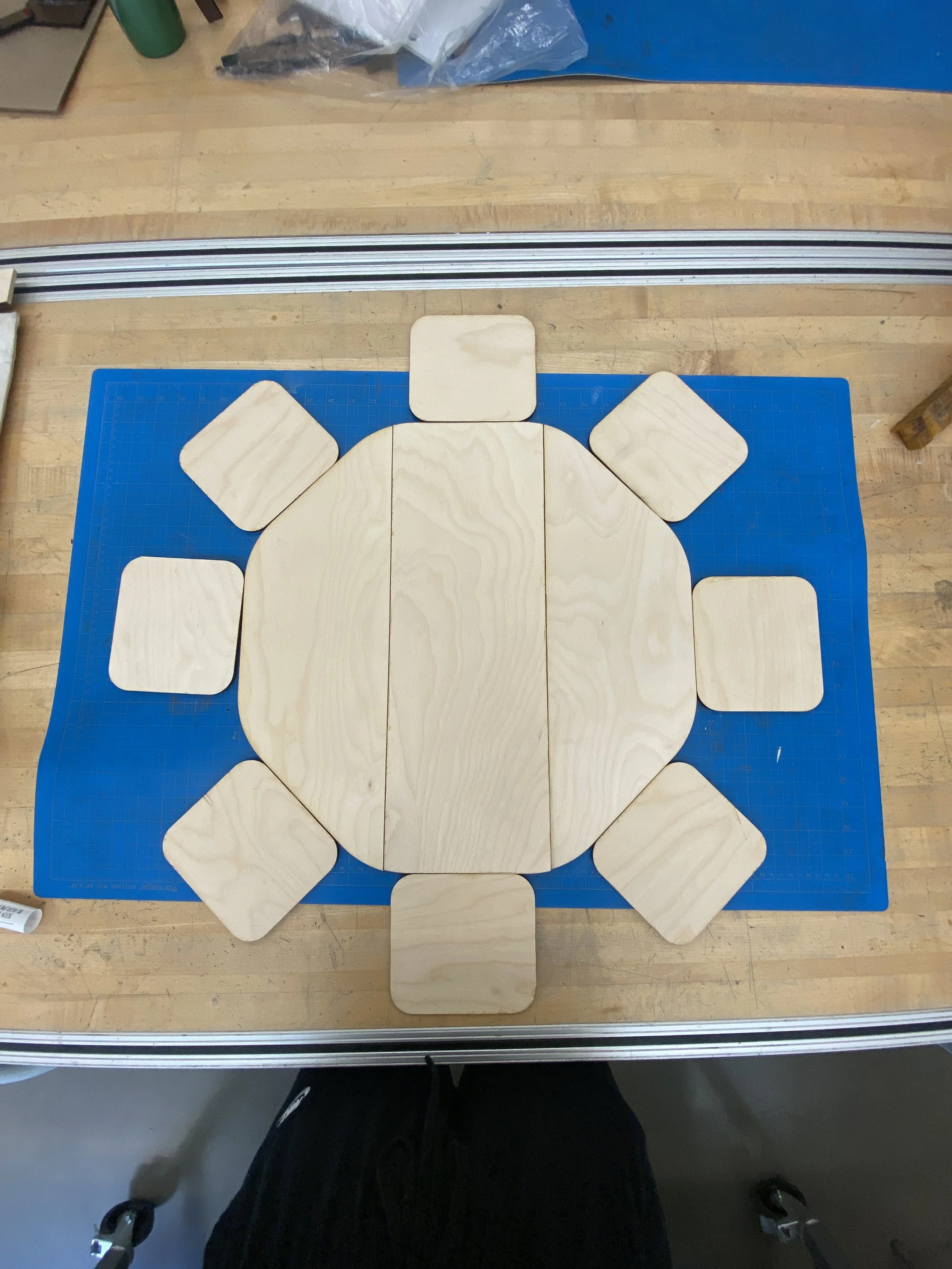 Wooden tiles arranged in a circle on a blue cutting mat, on a wooden workbench.