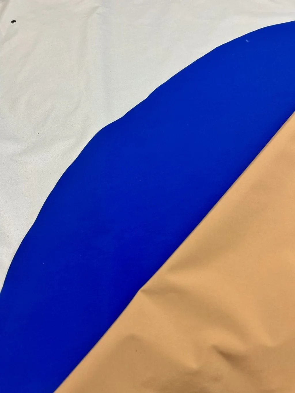 Close-up of a fabric with a large blue curved stripe on a beige and white background.