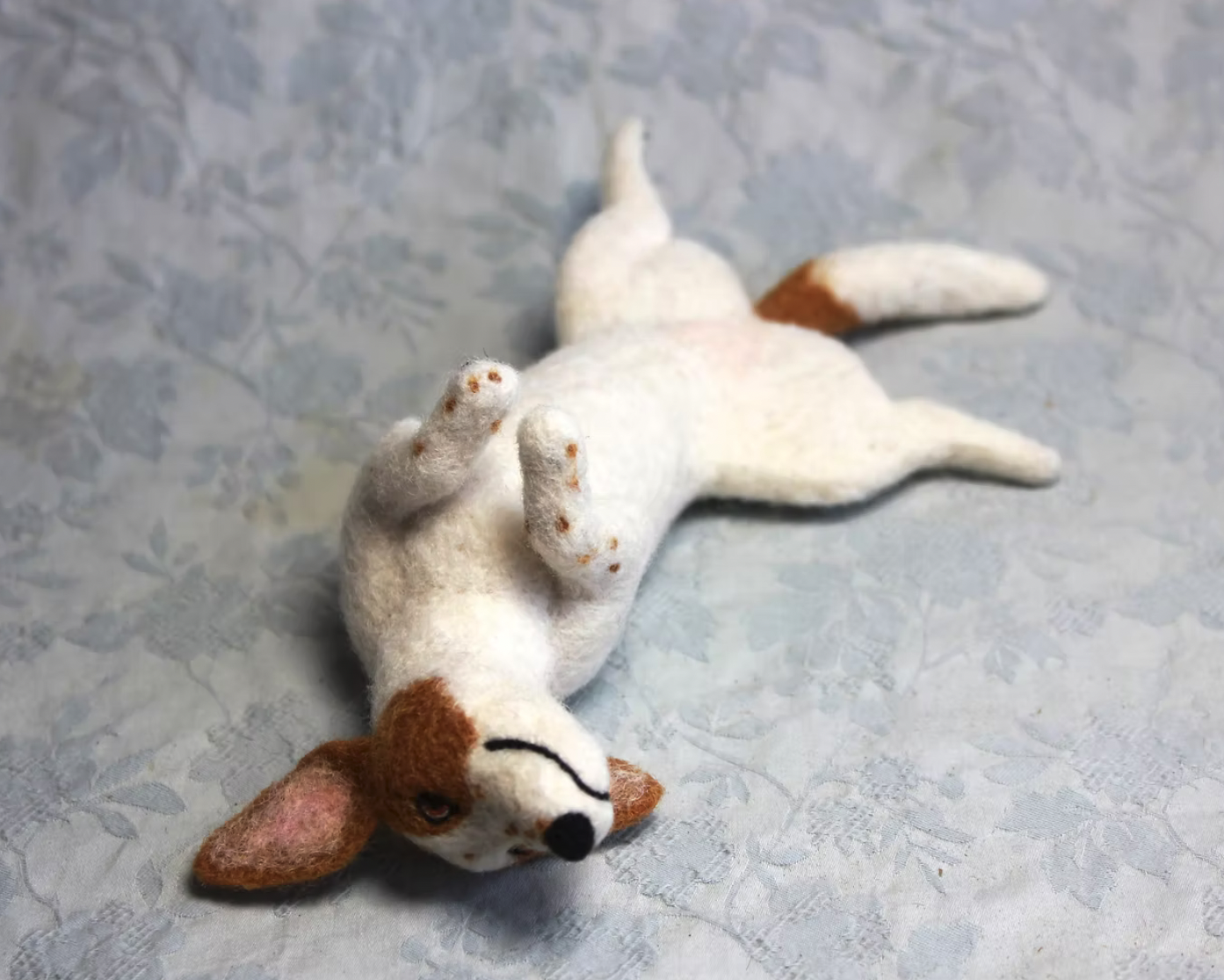 Felted dog toy lying on its back on a light gray textured surface.