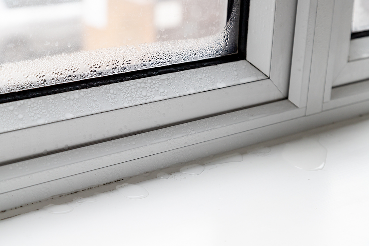 Close-up of a window with water droplets and condensation, with water dripping onto a white surface below.