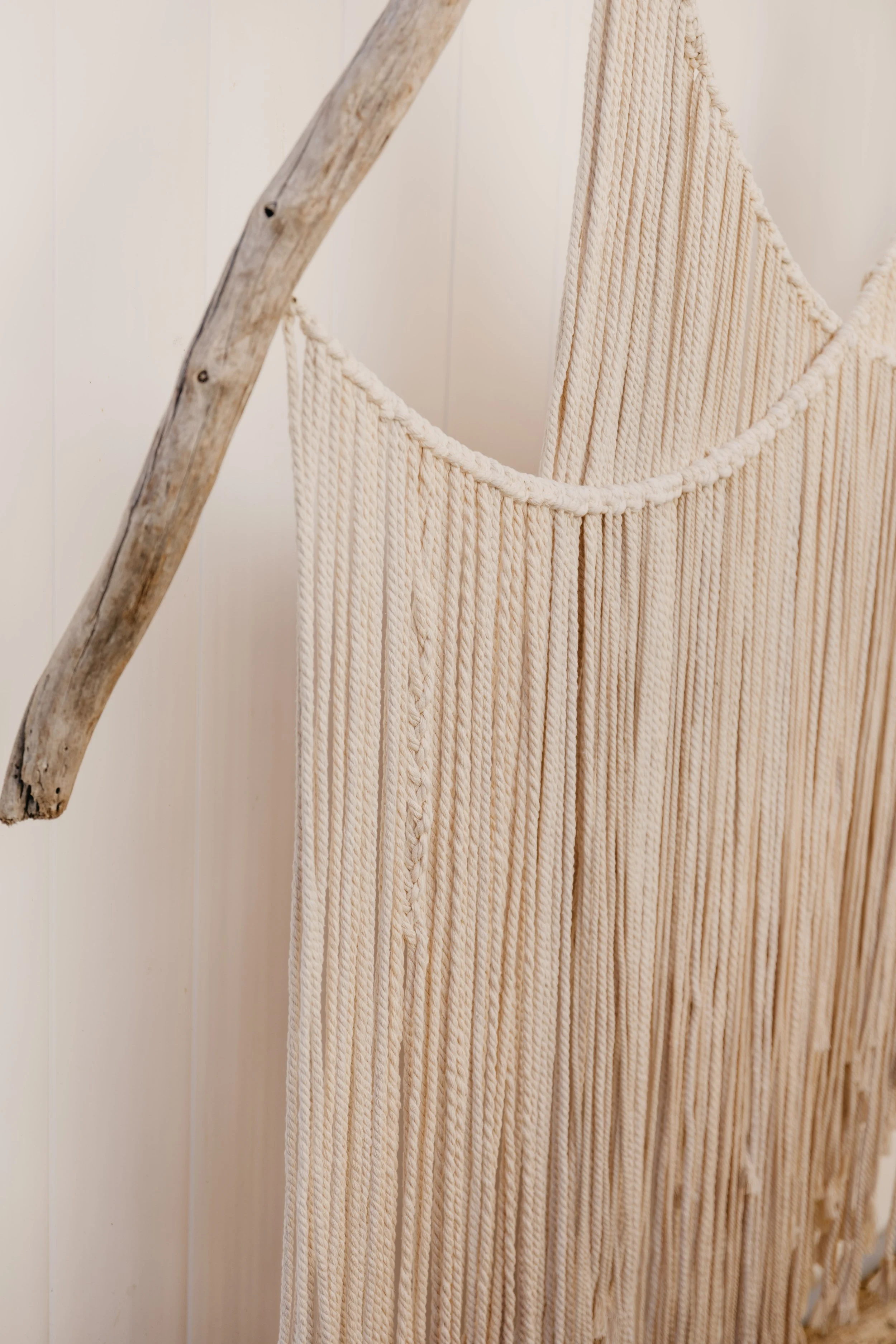 A close-up of a decorative wall hanging made of cream-colored chunky knit ropes, attached to a weathered wooden branch.