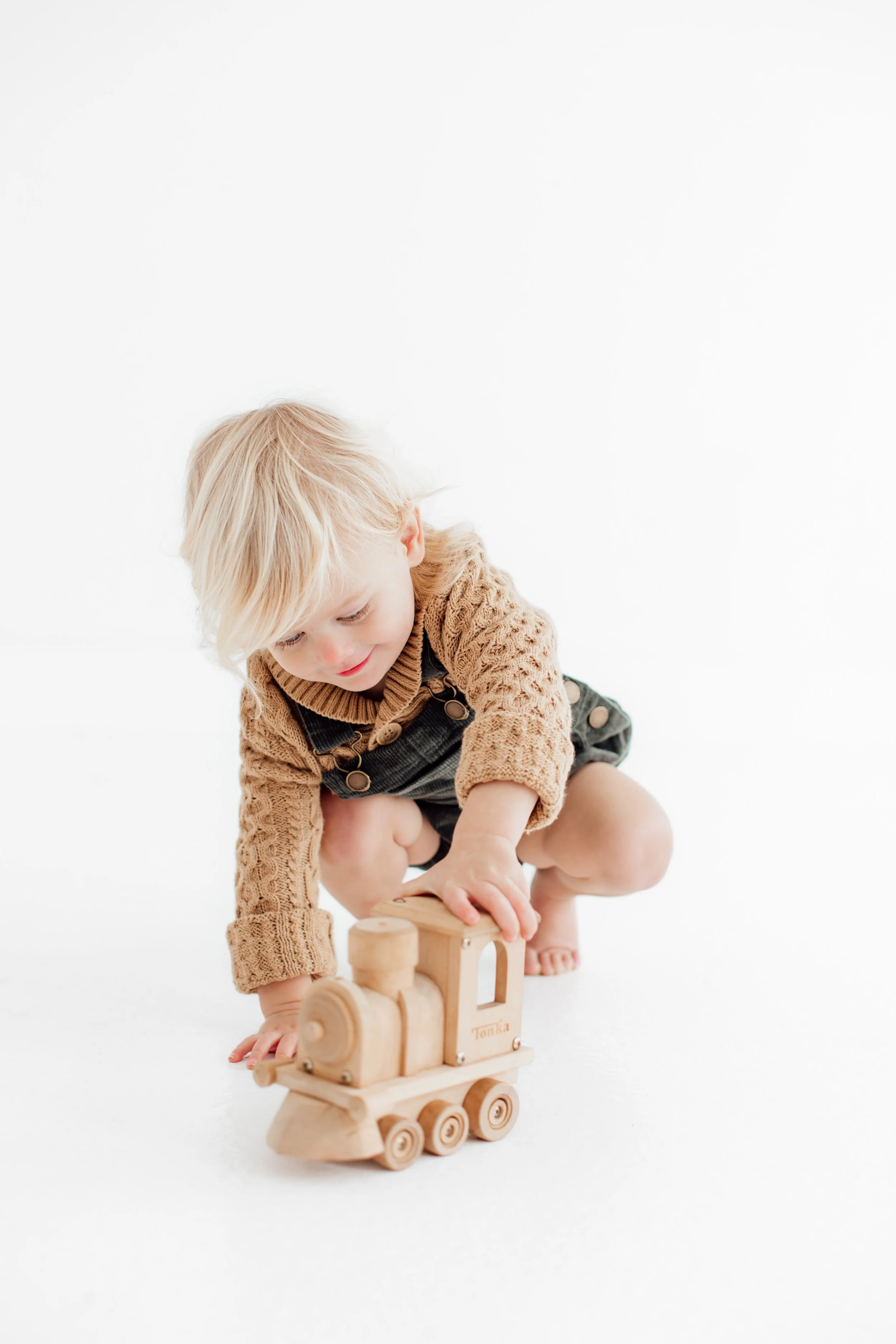 Young boy playing with a wooden toy train on a white background.