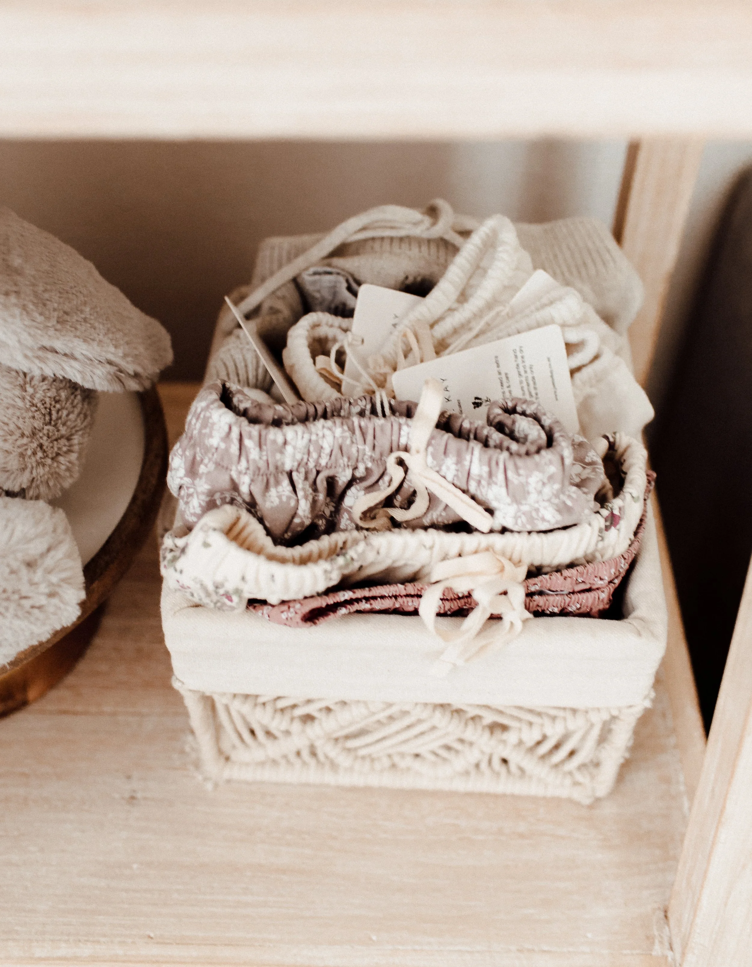 A basket containing folded baby clothes with tags, placed on a wooden shelf.