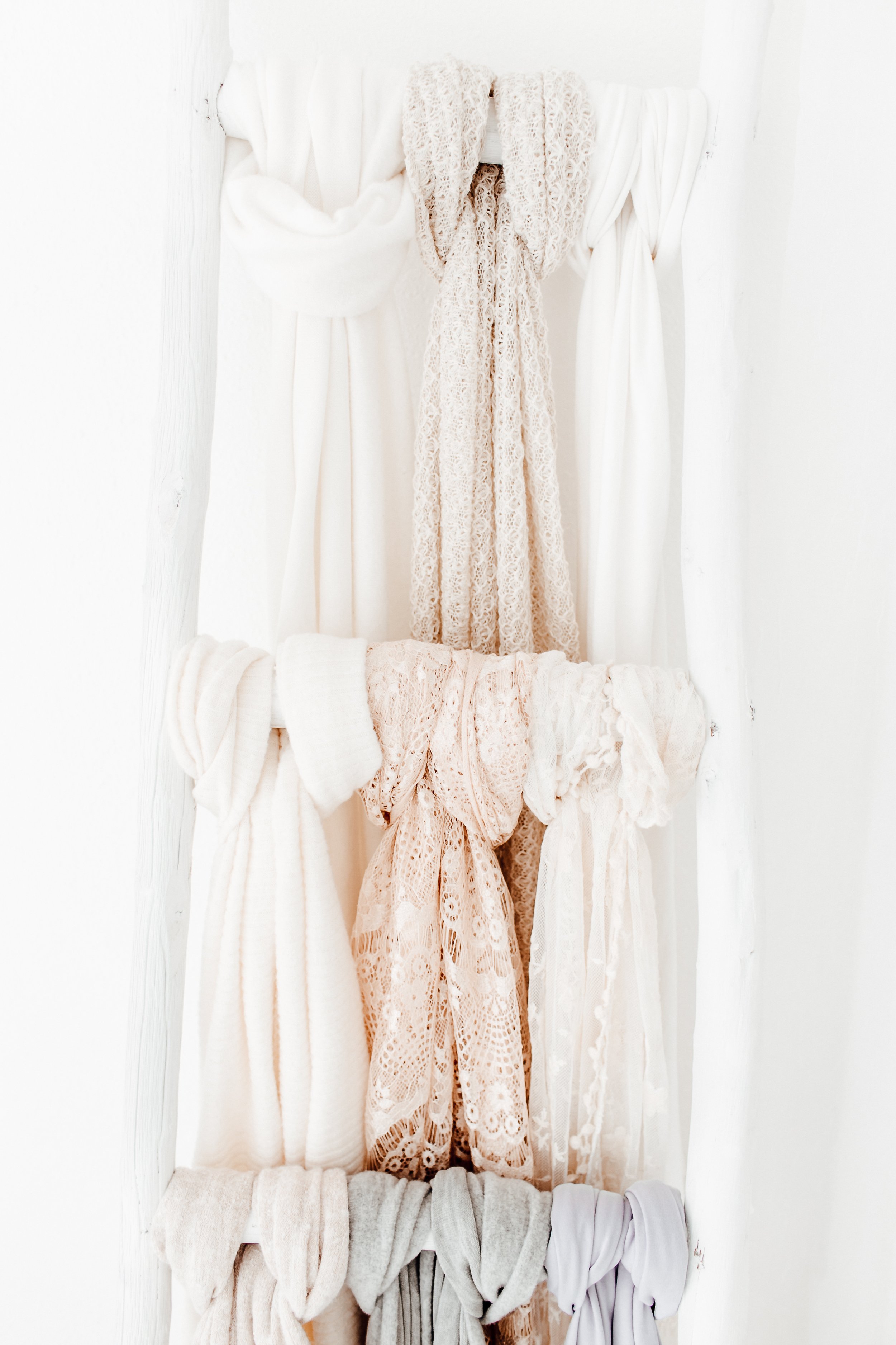 Multiple scarves and shawls in neutral tones hanging on a white wall