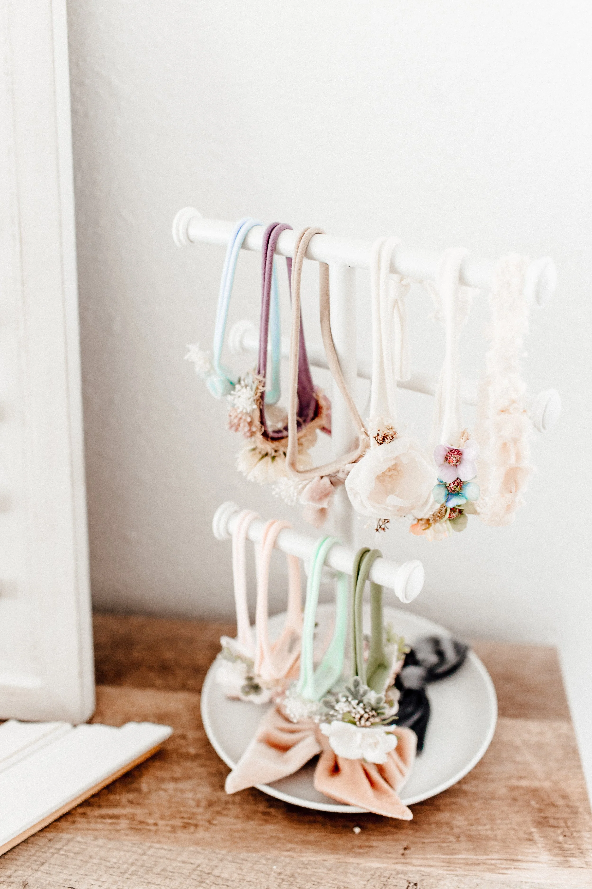 Decorative hairbands with floral and lace details on a white jewelry stand on a wooden surface.
