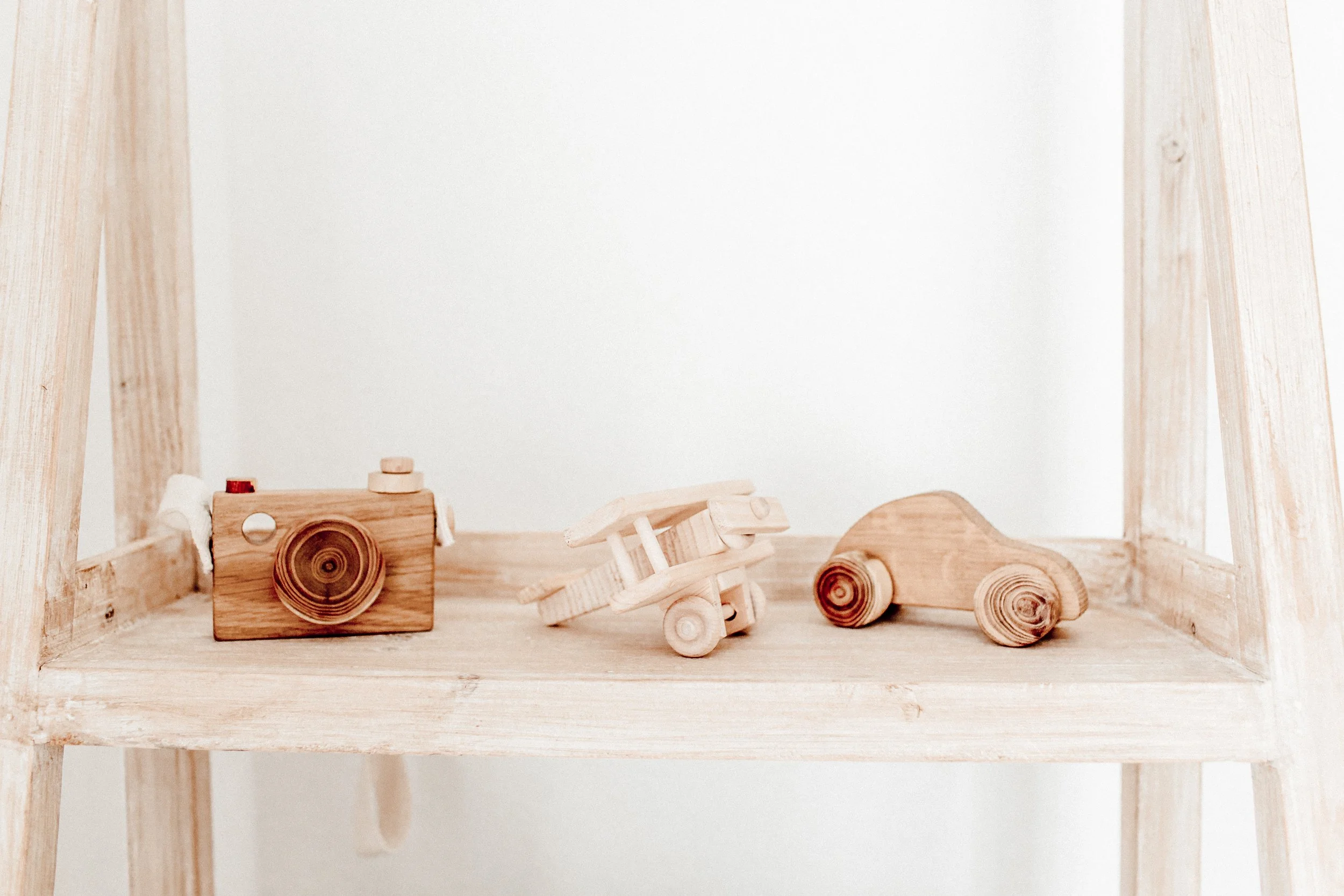 Three small wooden toy vehicles placed on a light-colored wooden shelf against a white background.