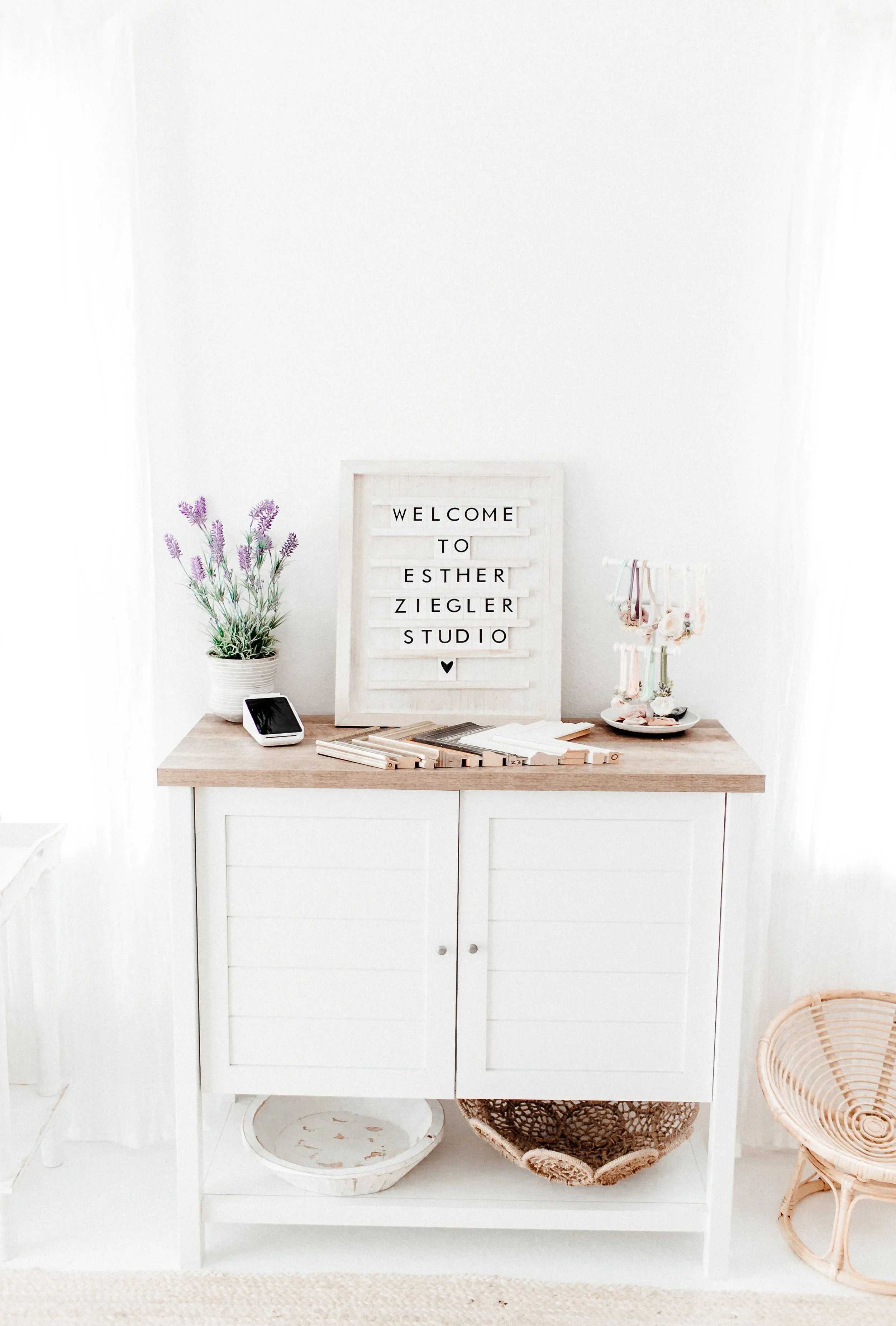 White cabinet with a wooden top, decorative lavender plant, smartphone, and sign that reads "Welcome to Esther Ziegler Studio".