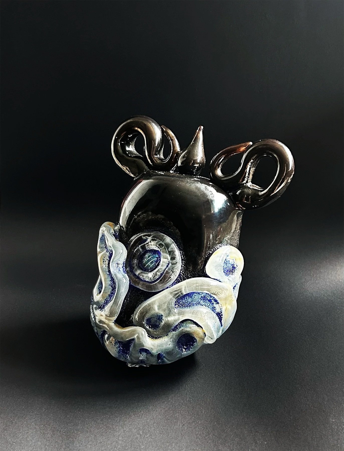A glass robot with a metallic black head and decorative white and blue swirled details, set against a black background.