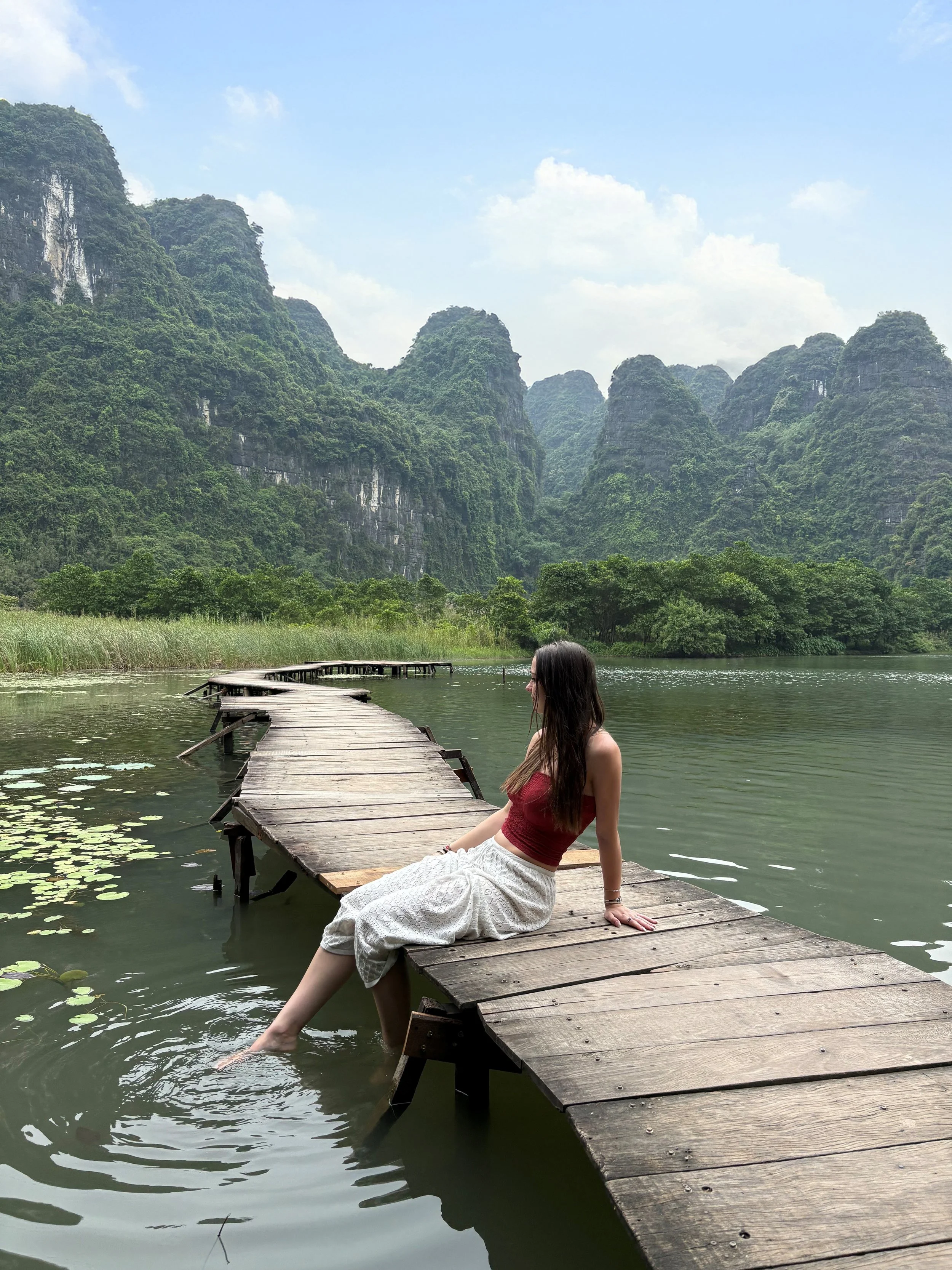 Jazz sitting on a wooden dock extending into a calm lake with green mountains and a partly cloudy sky in the background.
