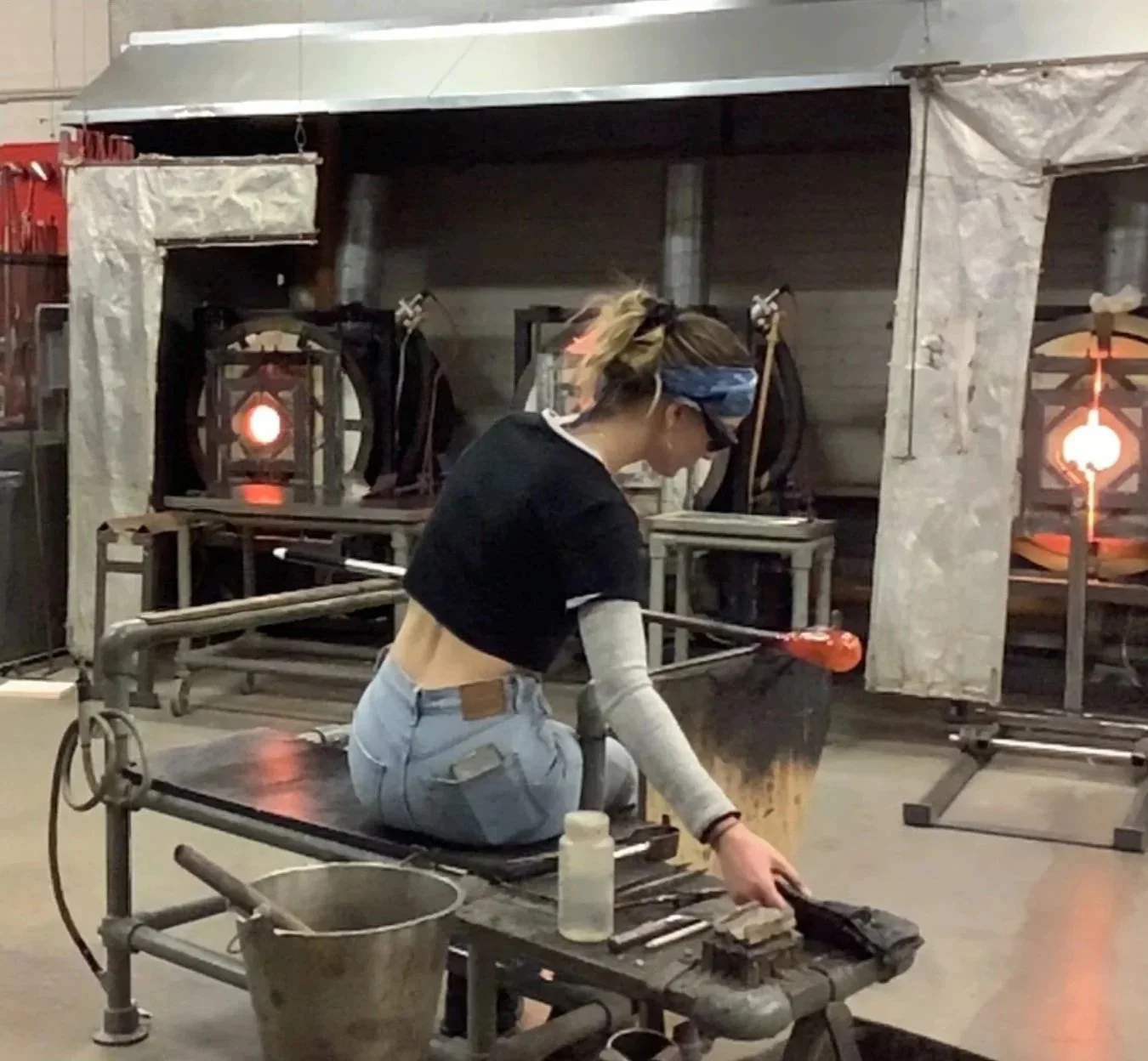 Jazz working with glass in a glassblowing workshop, shaping molten glass with tools.