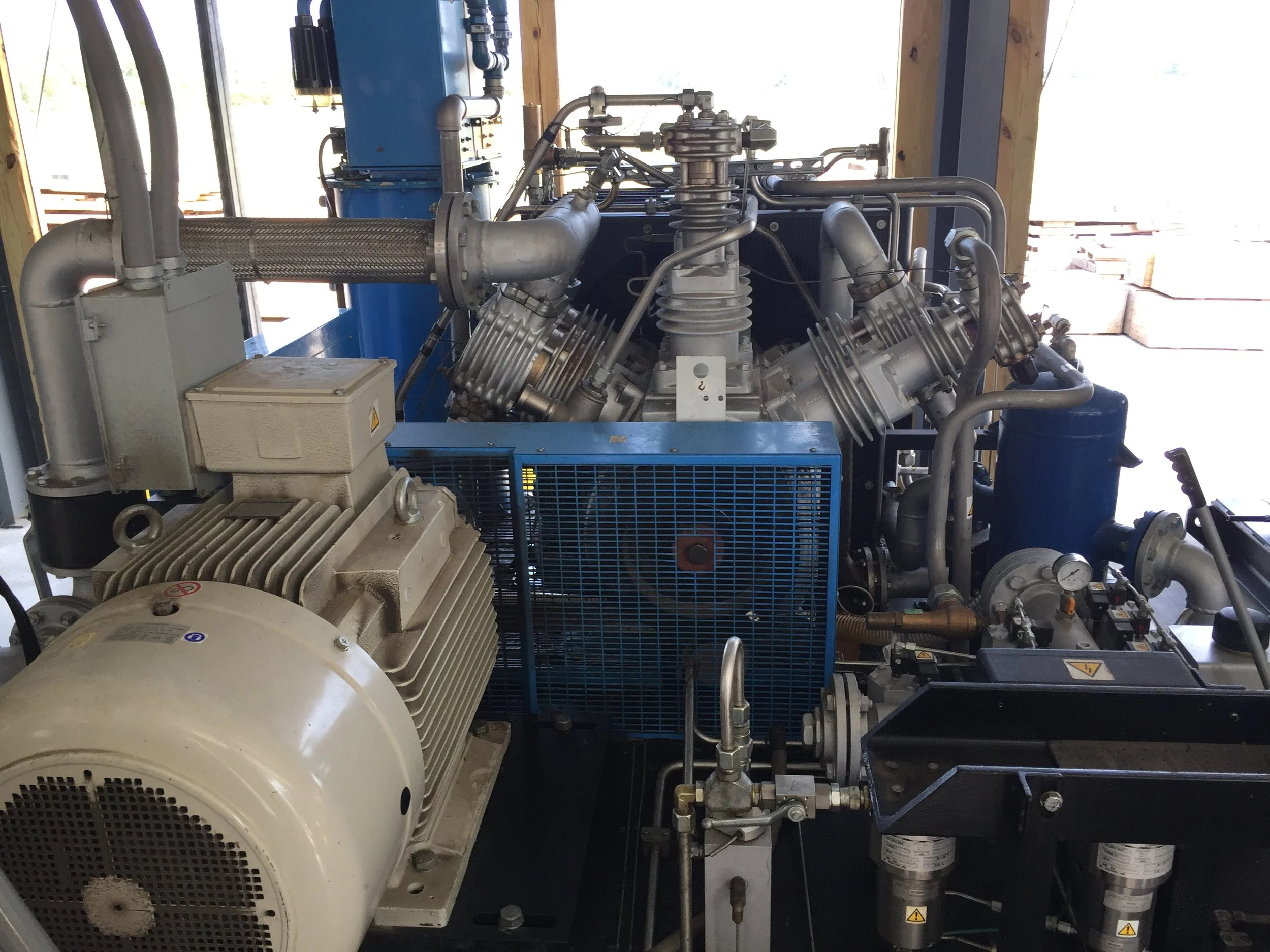 Industrial machinery with a large white motor, a blue protective cage, and metal pipes and components.