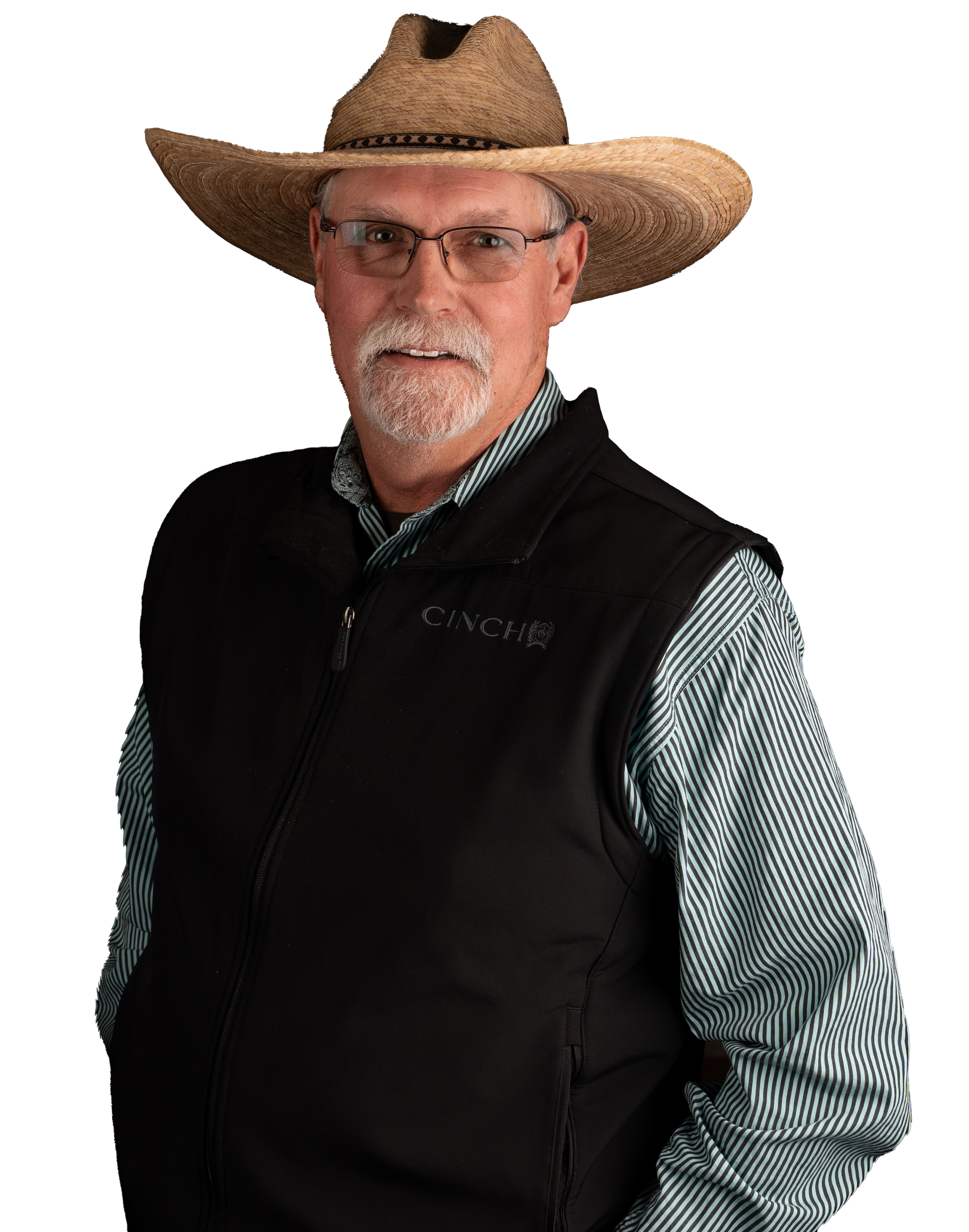 A man with glasses, a white beard and mustache, wearing a tan straw hat and a black vest over a striped shirt, standing against a black background.