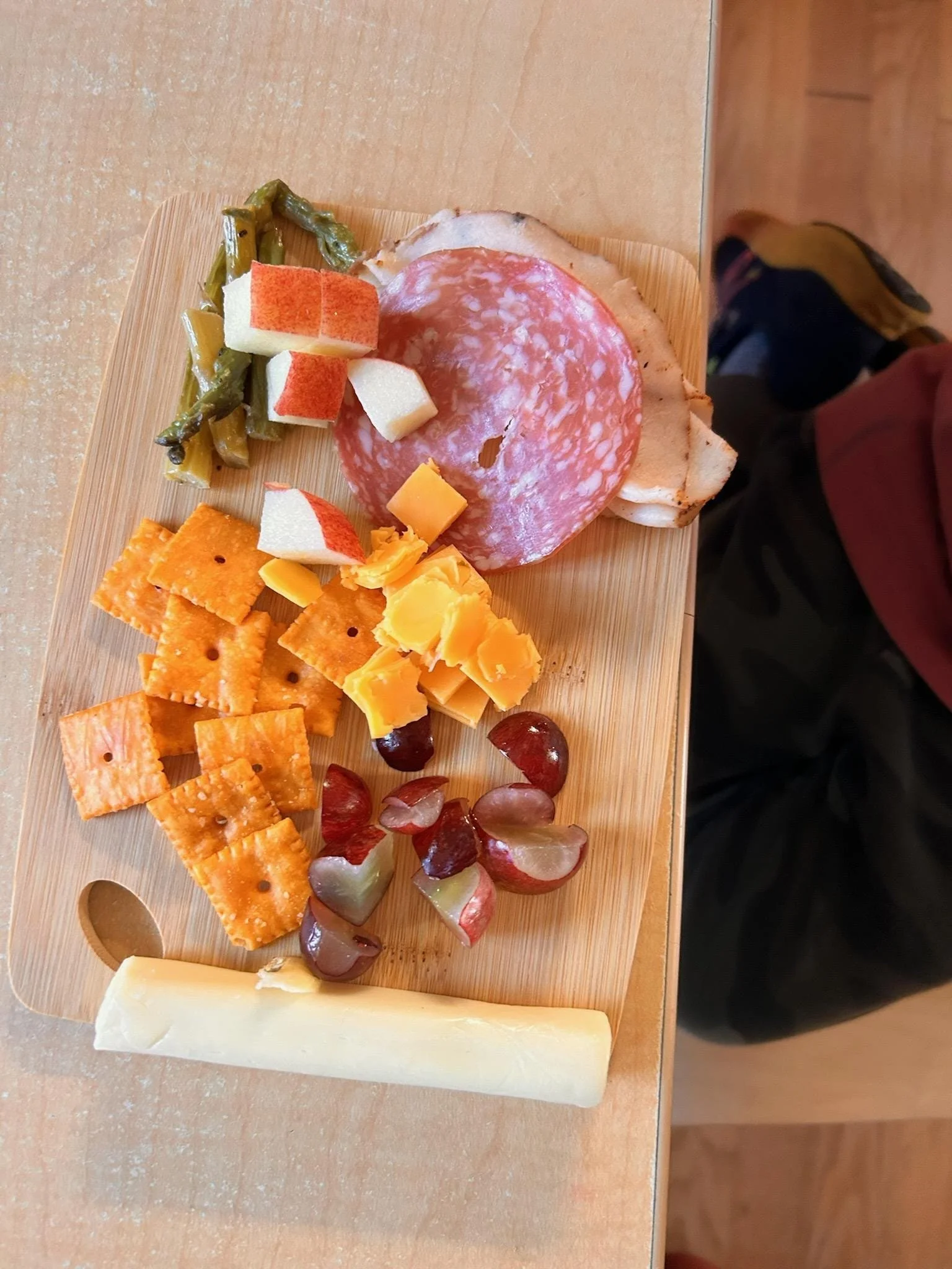 A snack board with cheese, grapes, apples, sliced salami and turkey, asparagus, and crackers