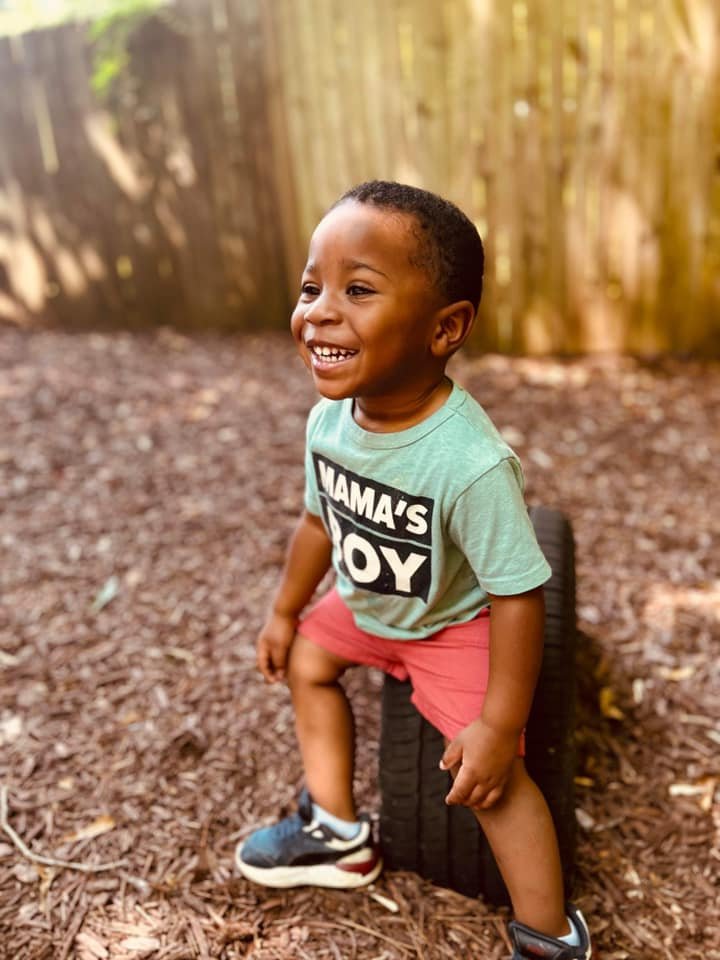 A little boy sitting on a tire on a playground smiling