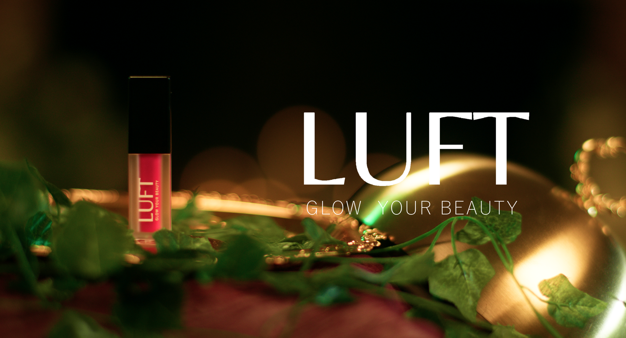 Close-up of a pink lip gloss tube with a black cap and the text "LUFT" on it, surrounded by green leaves and blurred warm lights in the background, with the overlay text "LUFT Glow Your Beauty."