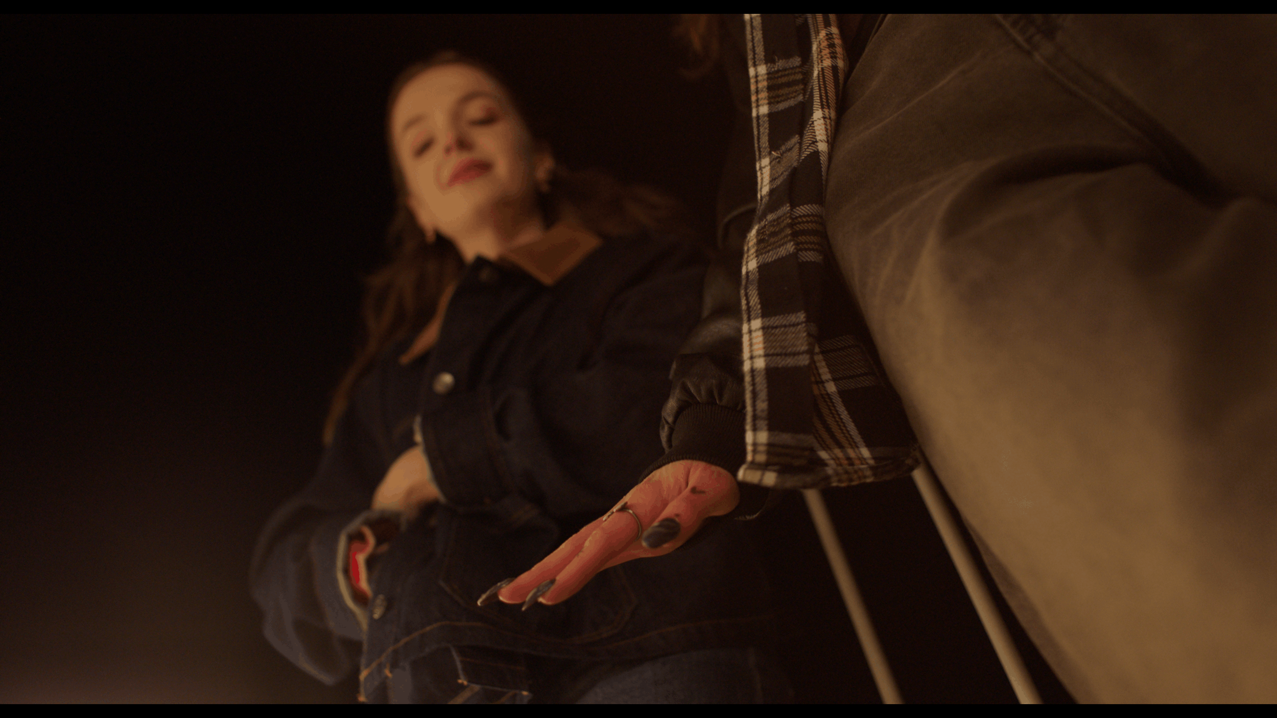 Low angle view of a woman with dark hair wearing a dark jacket, smiling, and reaching out with her hand towards the camera.