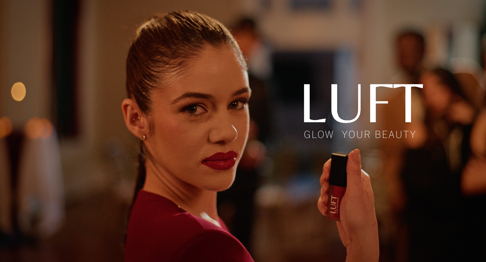 A woman with red lipstick and earrings holding a lipstick in a dimly lit social setting. The text 'LUFT GLOW YOUR BEAUTY' is overlaid on the image.